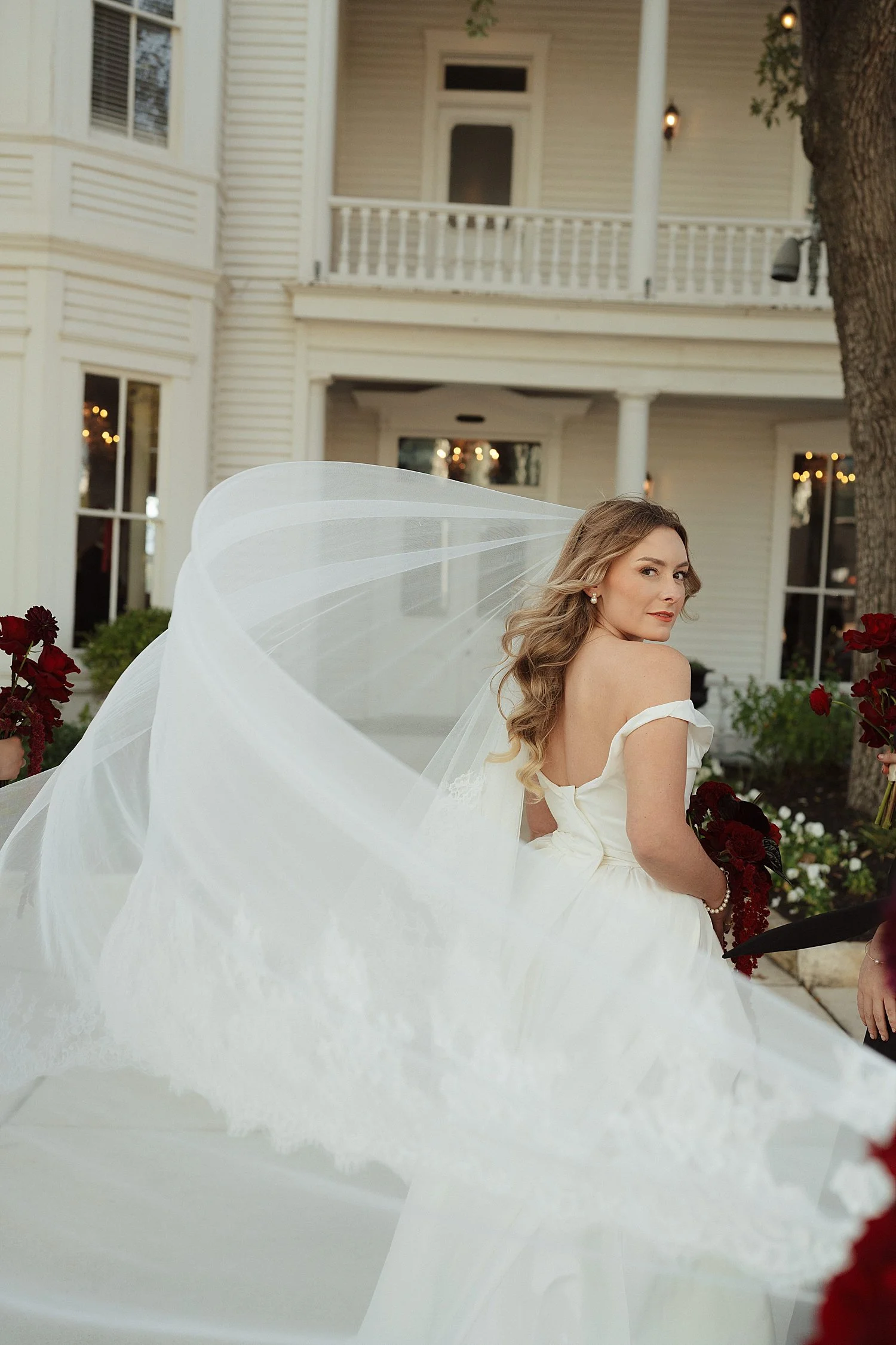  bride walks towards The Allan House with the wind whipping her veil  