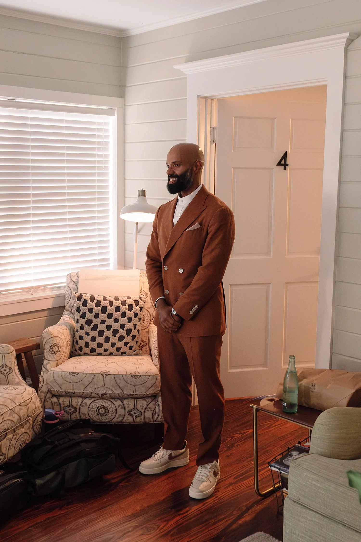  groom in rust color suit stands in getting ready suite by Austin wedding photographer 