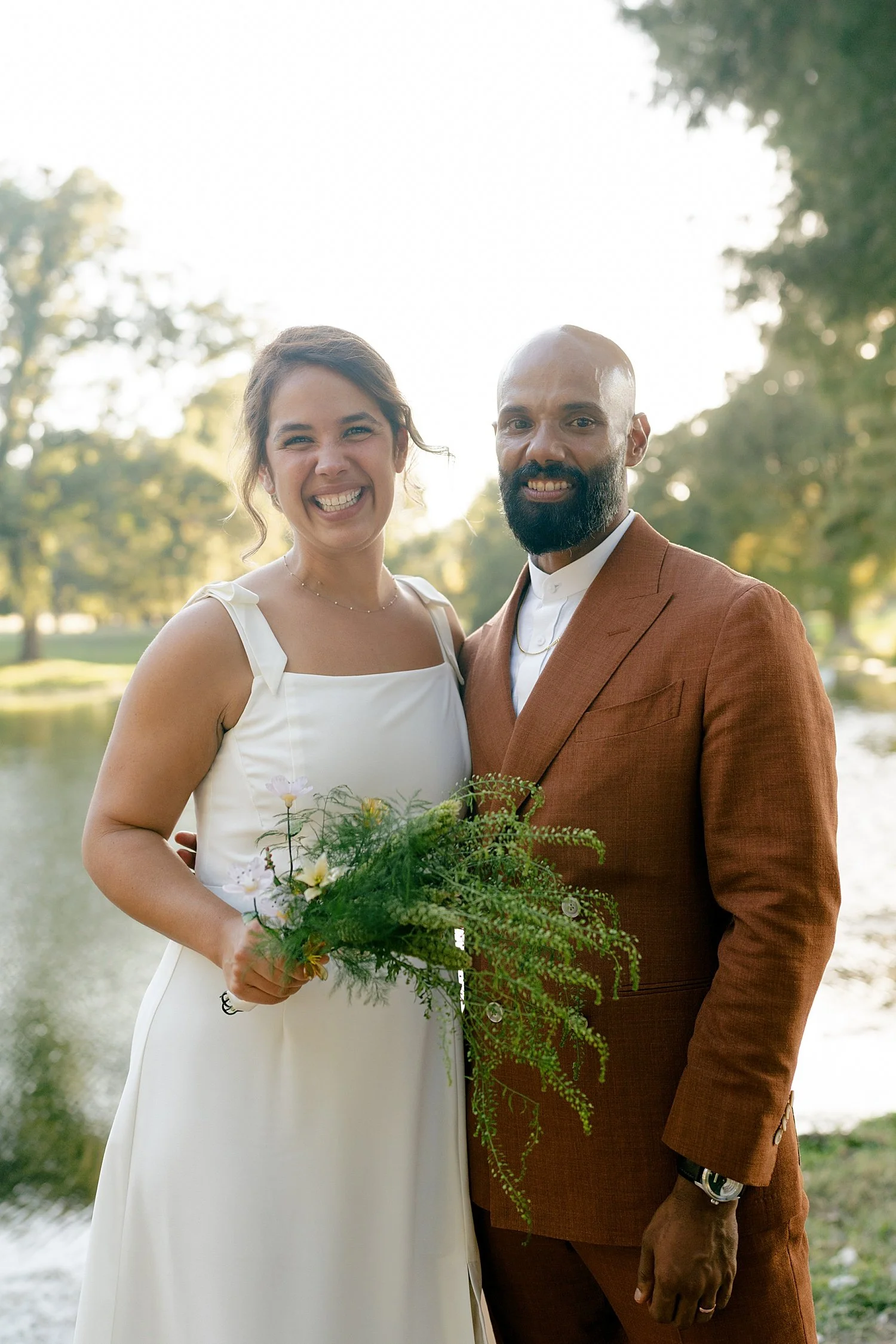  husband and wife grin together in front of lake at Springs Lake Ranch 