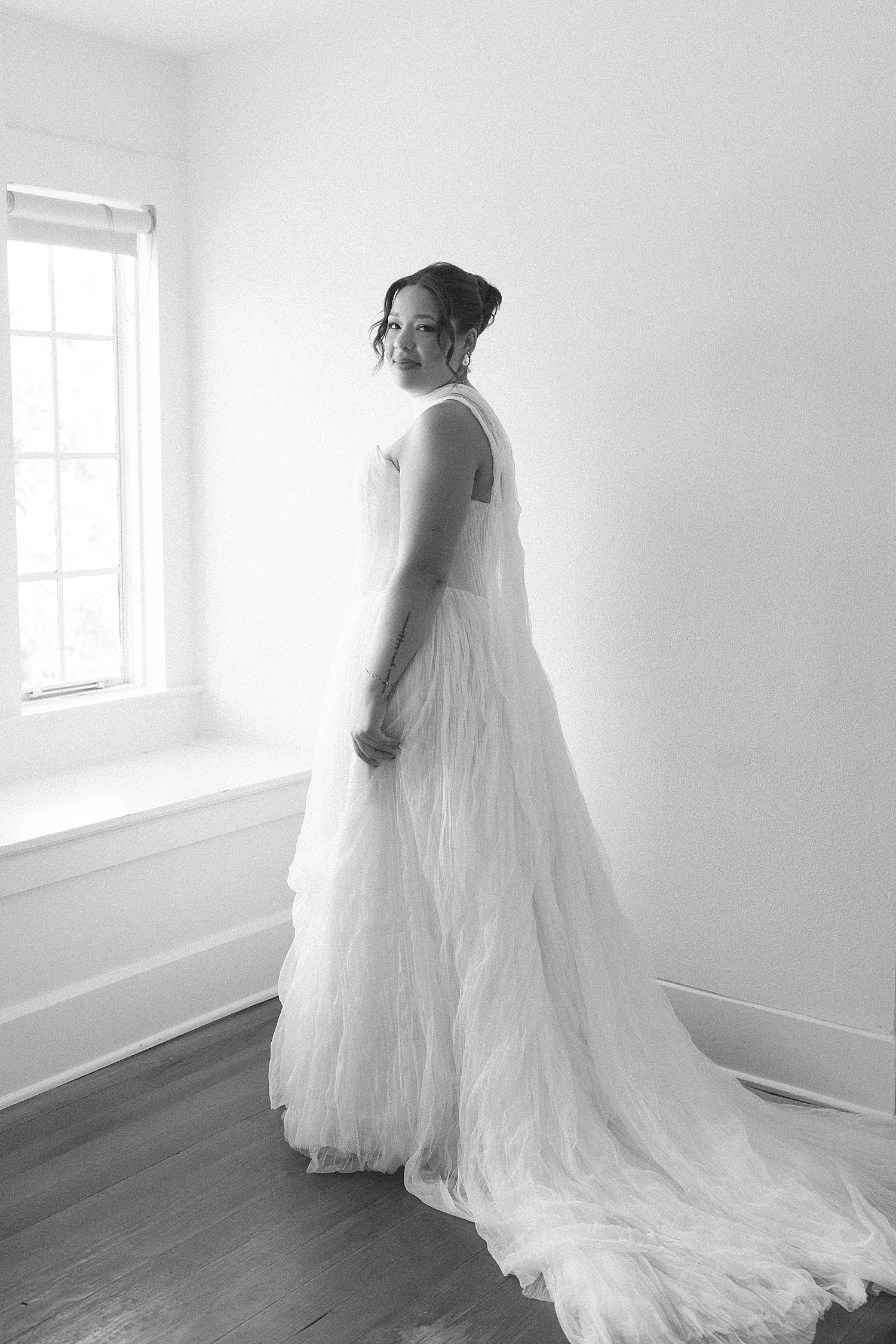  bride stands in front of large window in her gown at The Caroline  