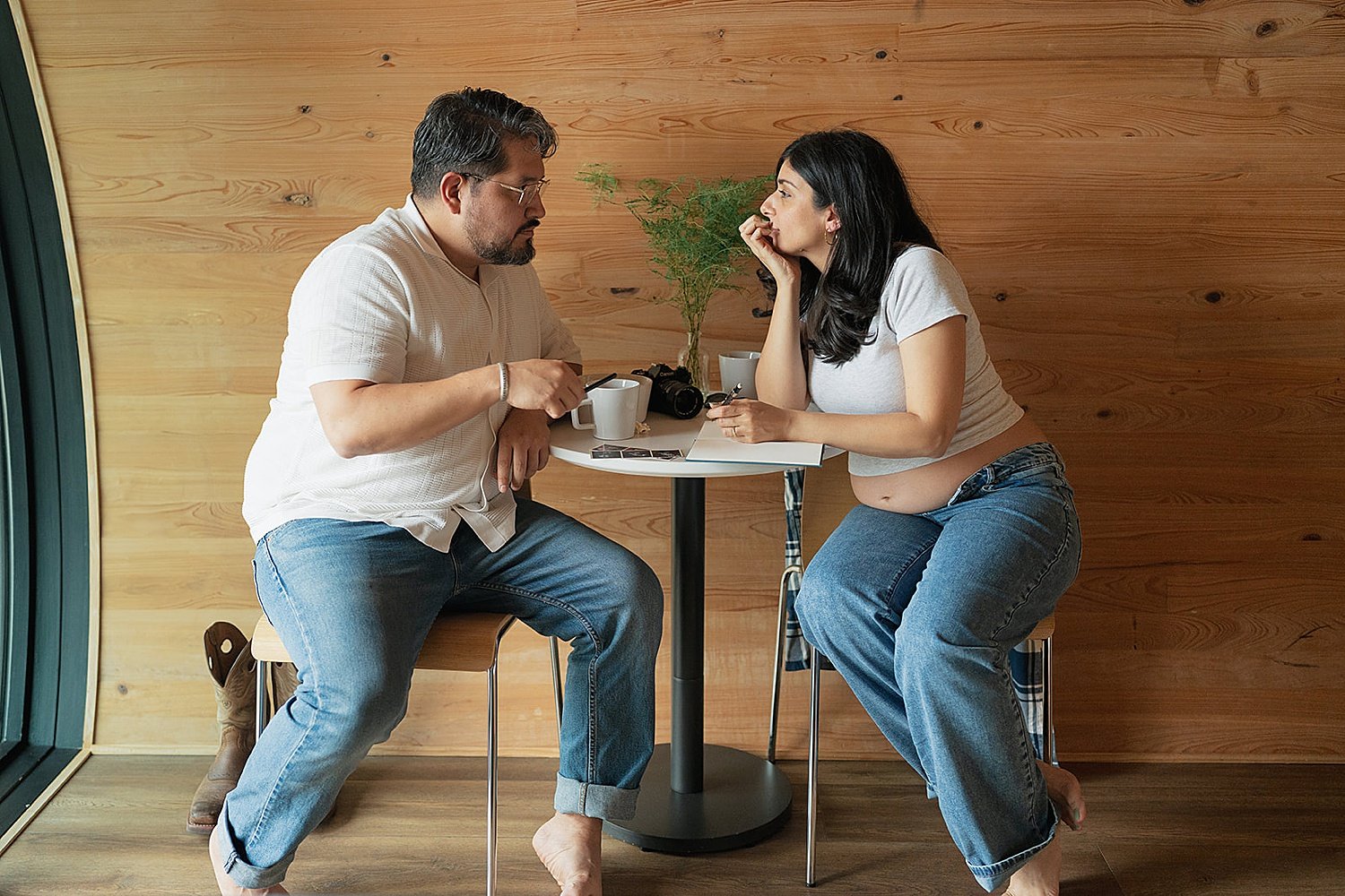  couple sits to drink coffee over a table for their babymoon photo session 