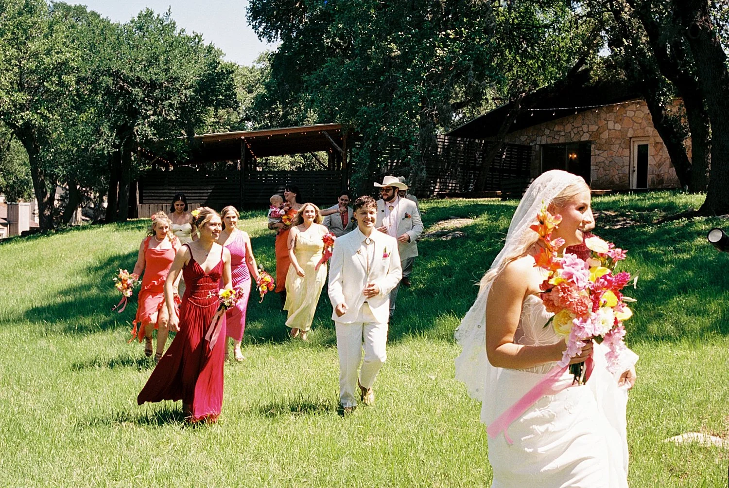  wedding party in bright dresses and tan suits follows newlyweds for colorful wedding celebration 