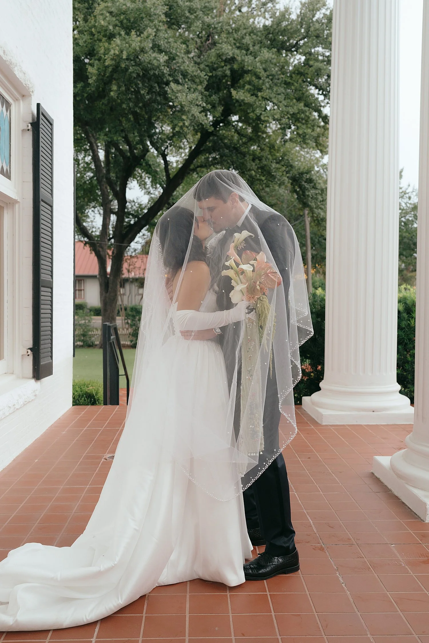  newlyweds snuggle under veil on porch by Jessica Joseph Photography 