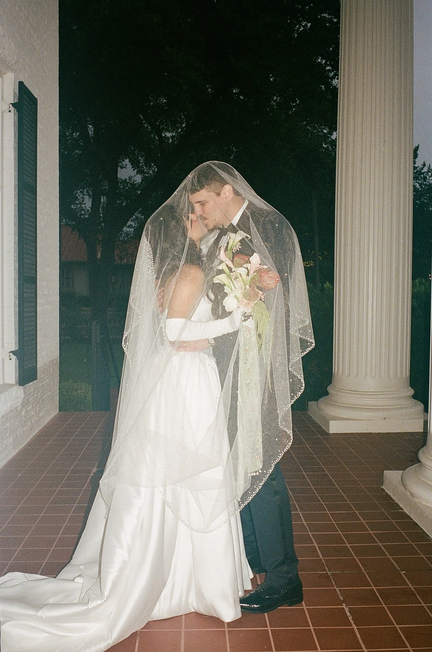  husband and wife stand on porch in rain under veil at Woodbine Mansion 