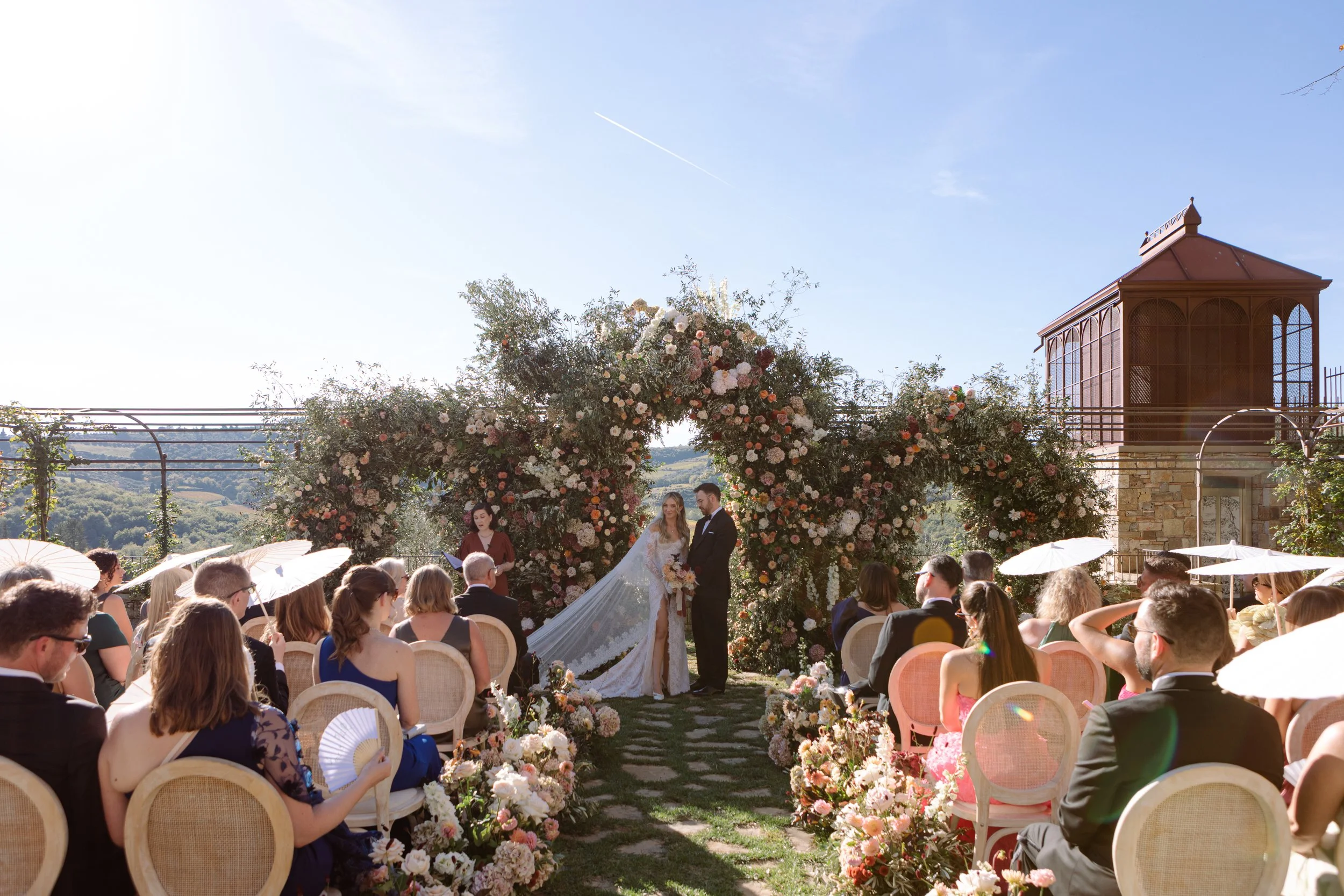 bride and groom under triple floral arch at their wedding ceremony in Tuscany Italy. Planned by destination wedding planner In Awe Weddings & Events