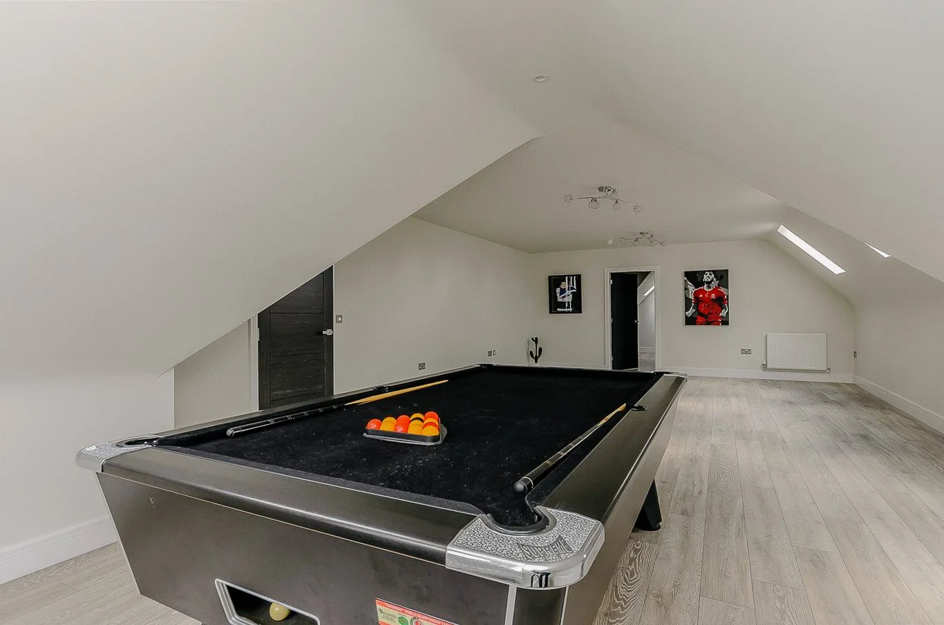 Modern loft with a pool table, wooden flooring, slanted ceiling, and sports posters on the walls.