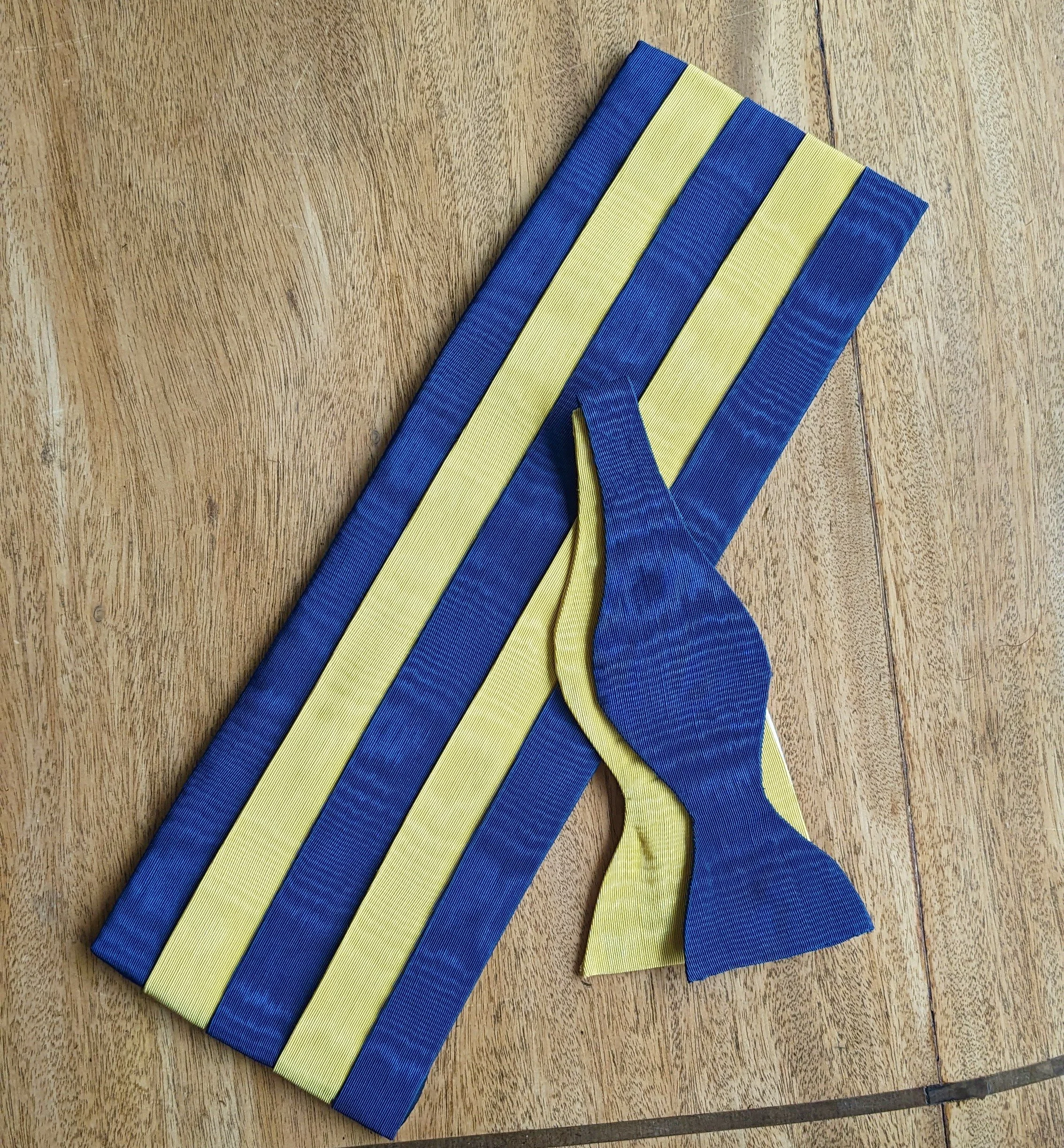 A yellow and blue striped fabric called SAG with a tied knot on a wooden surface.