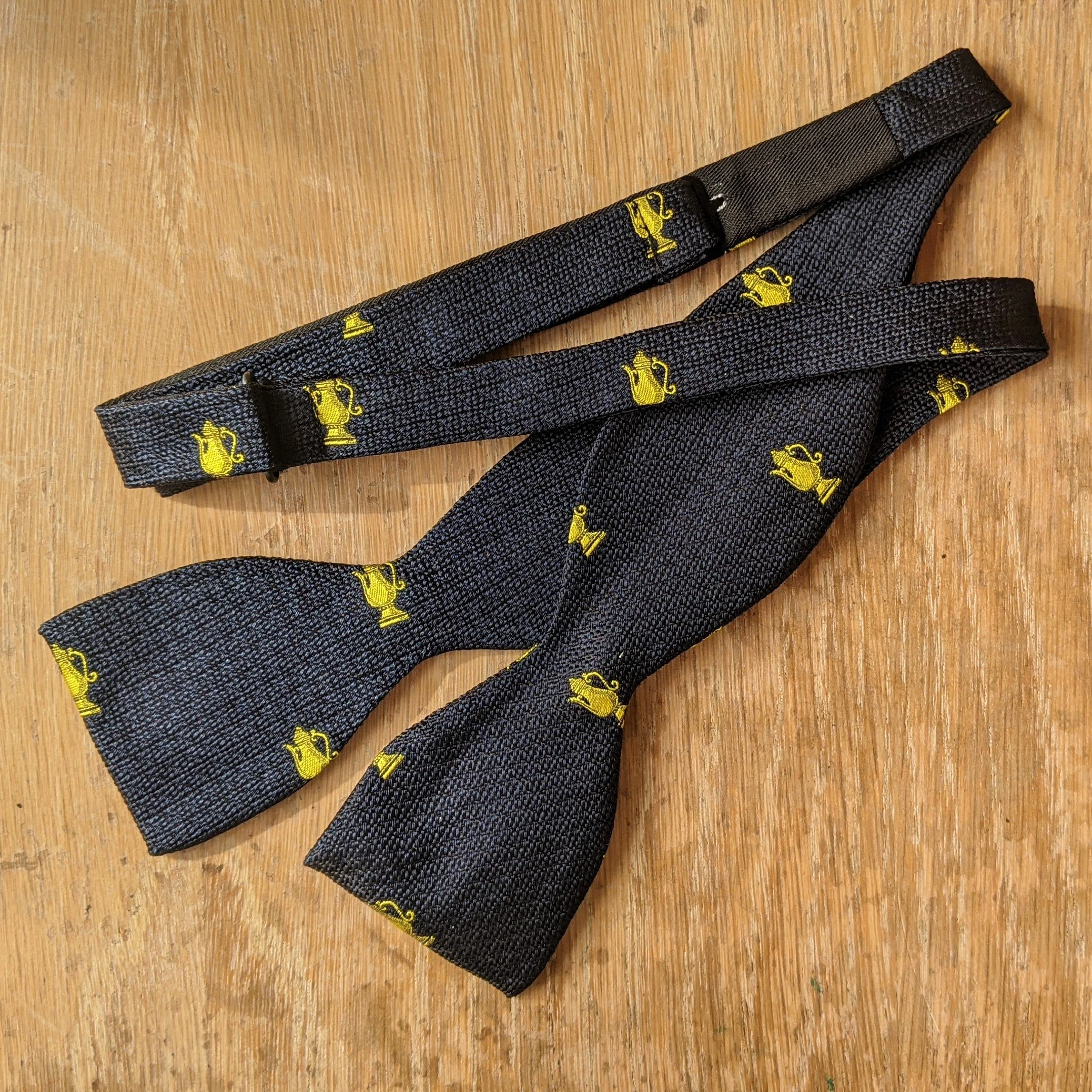 A black bow tie with yellow teapot and pitcher patterns on a wooden surface.