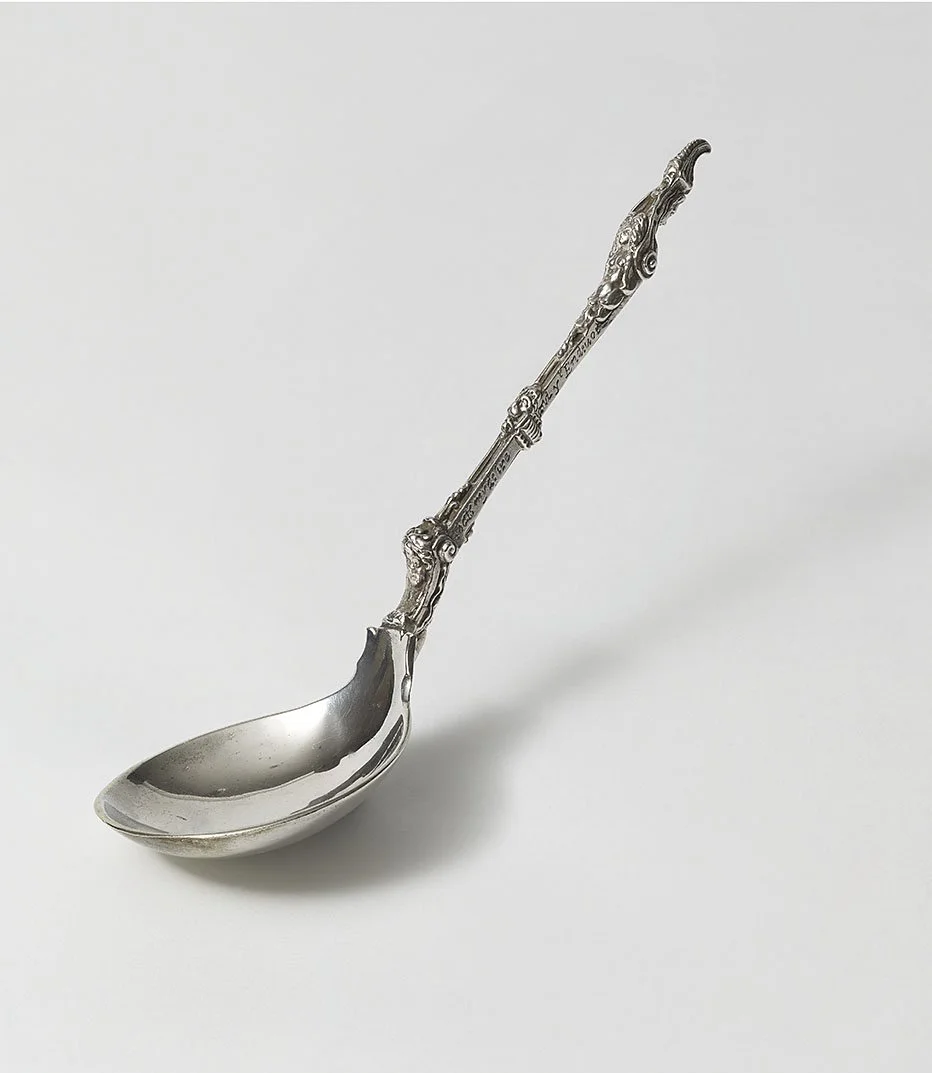 Silver teaspoon with an ornate, decorative handle on a plain white background.