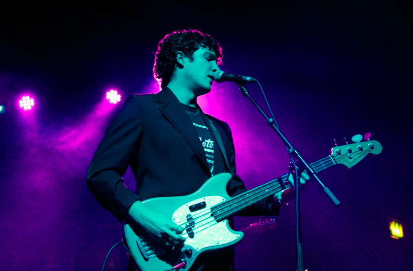 Park Hotel Band playing electric bass and singing into a microphone under purple stage lights
