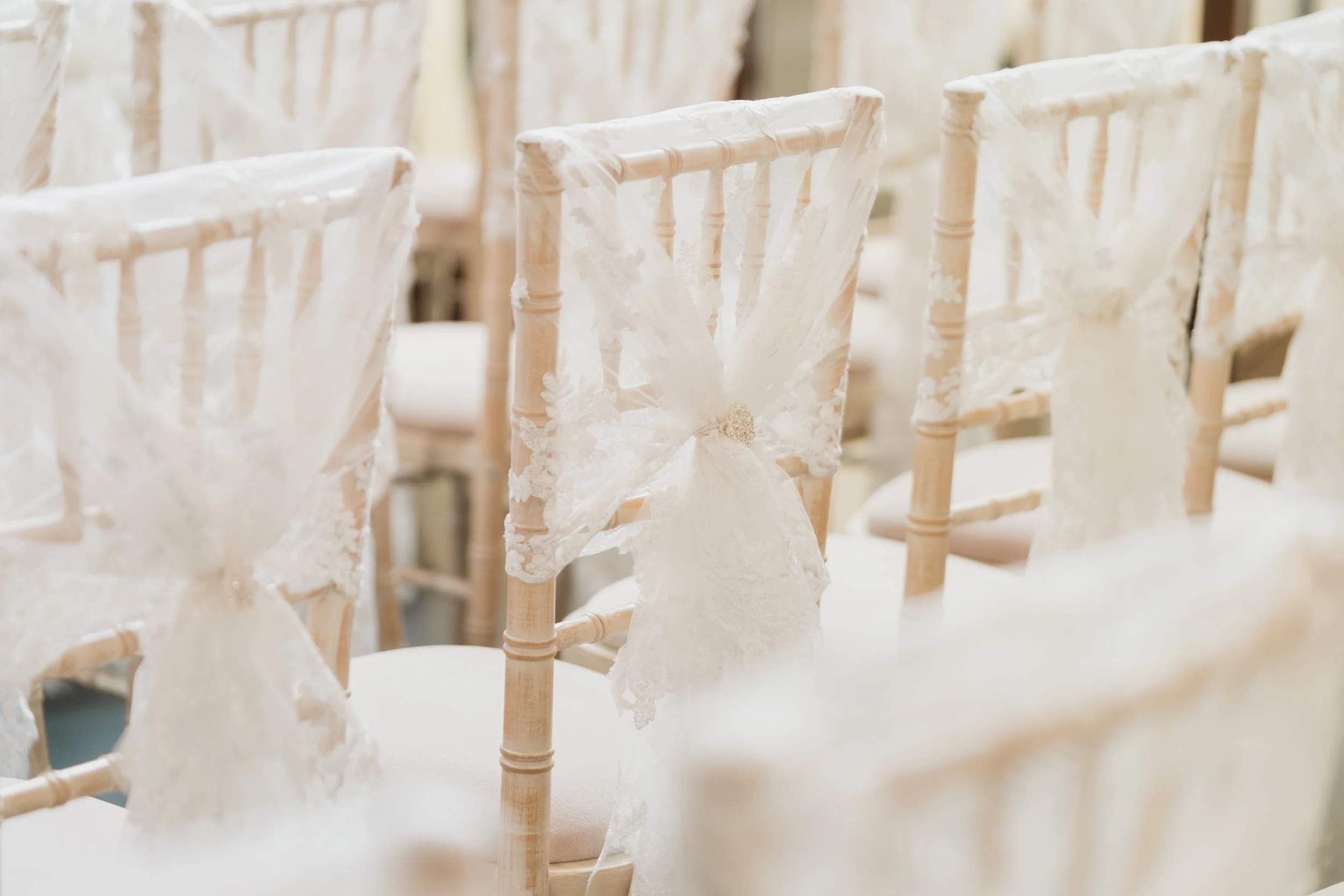 Rows of wooden chairs decorated with white lace and fabric bows, arranged for a wedding ceremony.