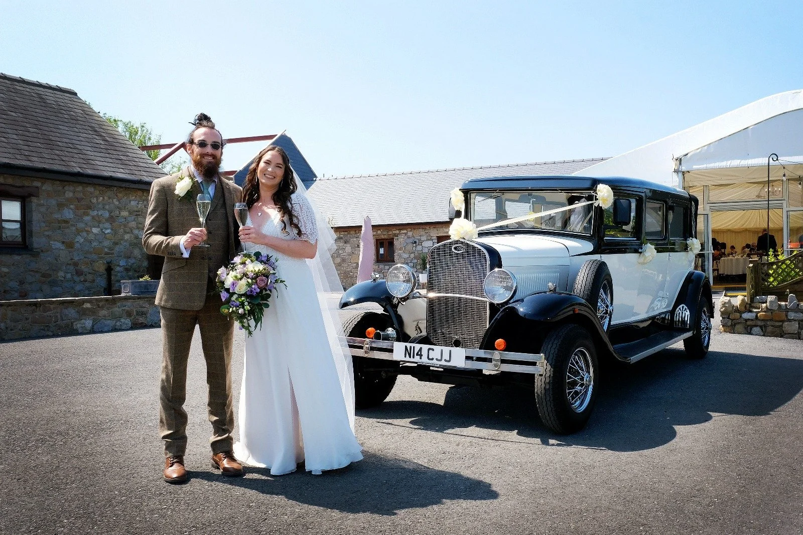 Bride and groom standing next to a vintage car decorated with flowers at their wedding celebration.