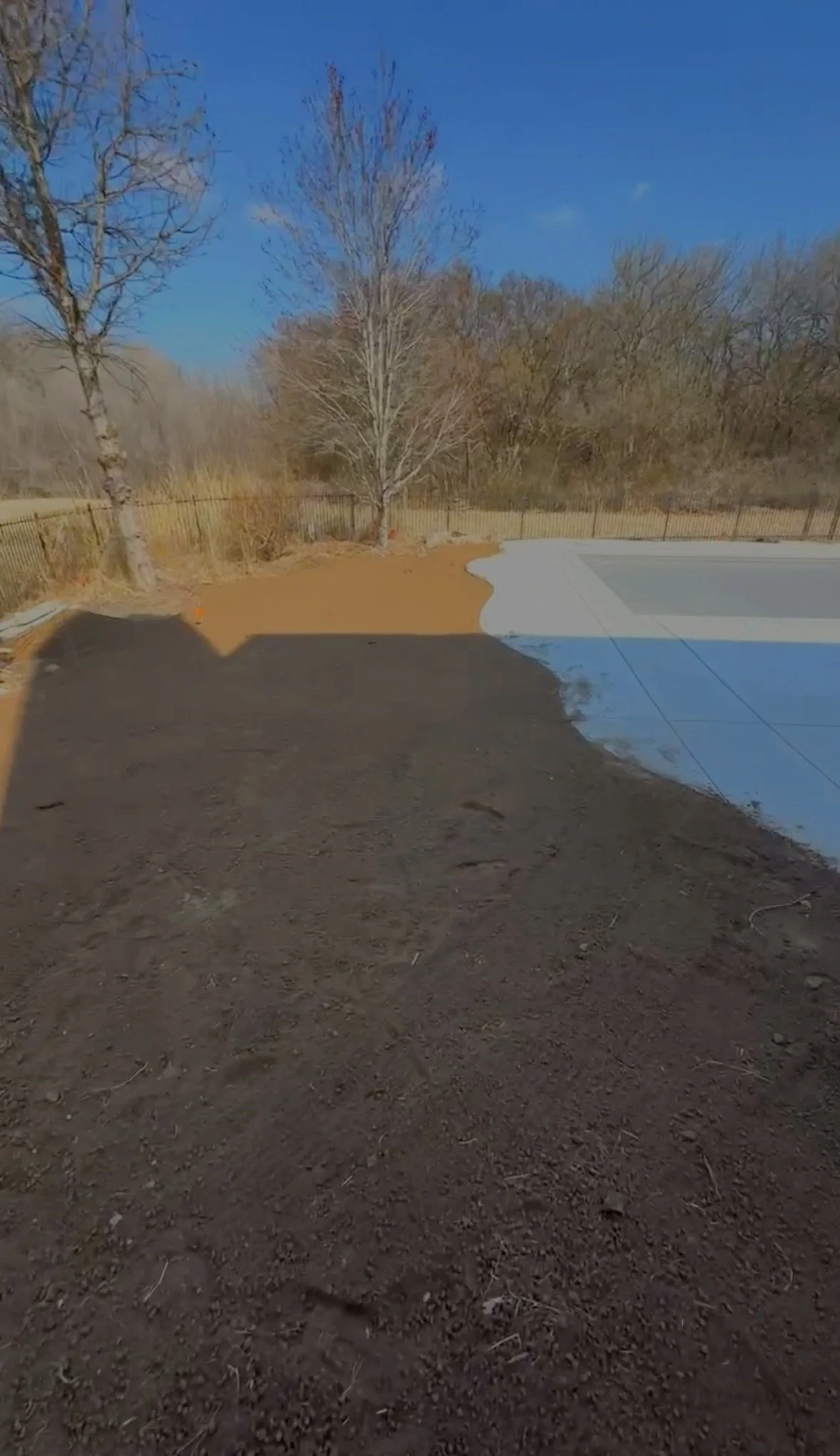 Backyard with bare trees, a fence, and a swimming pool; some part of the ground is freshly excavated and partially paved.
