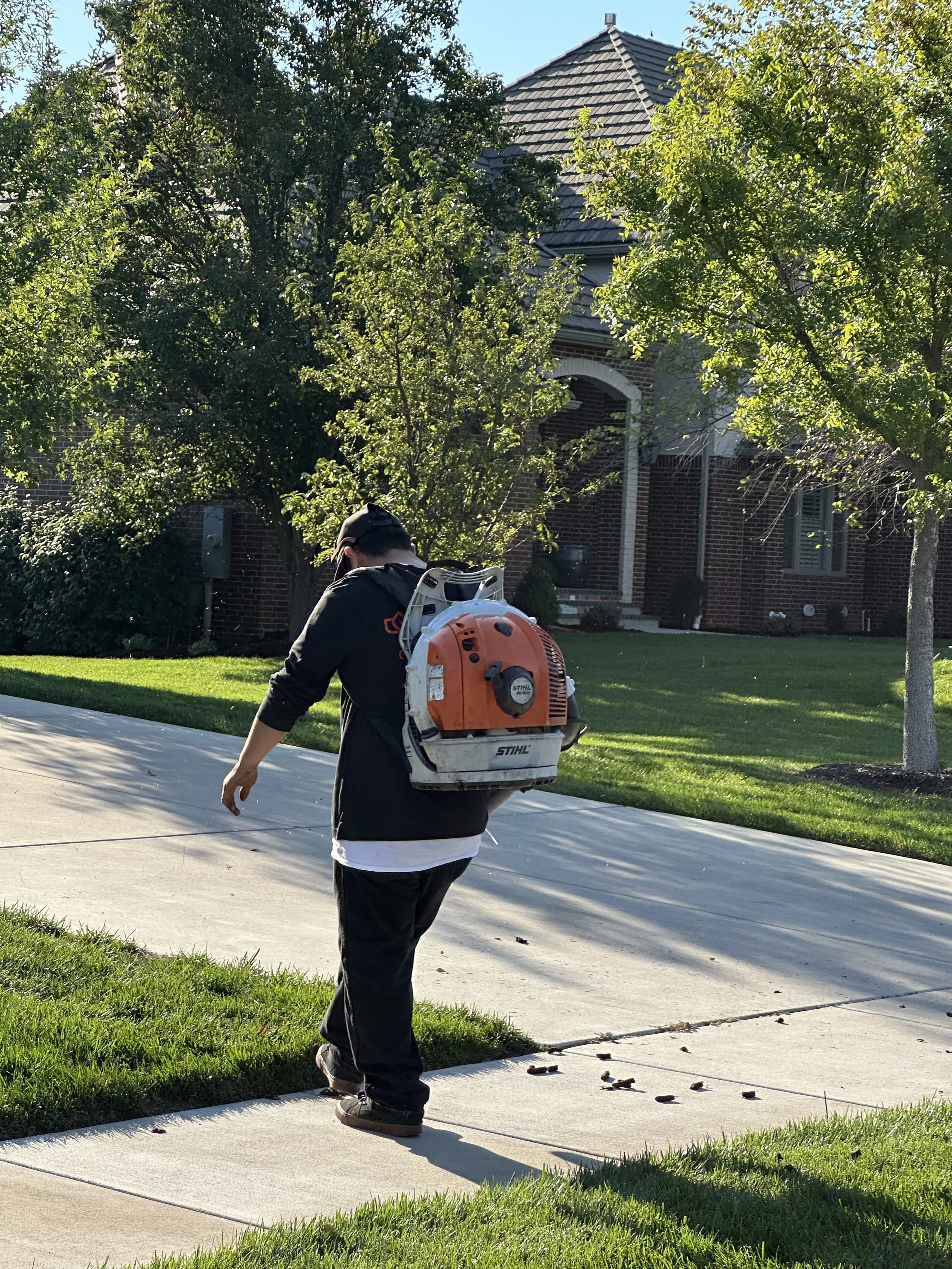Person walking with a leaf blower at a resedential lawn in wichita ks. Maintained by Goodman Lawn & Landscape.