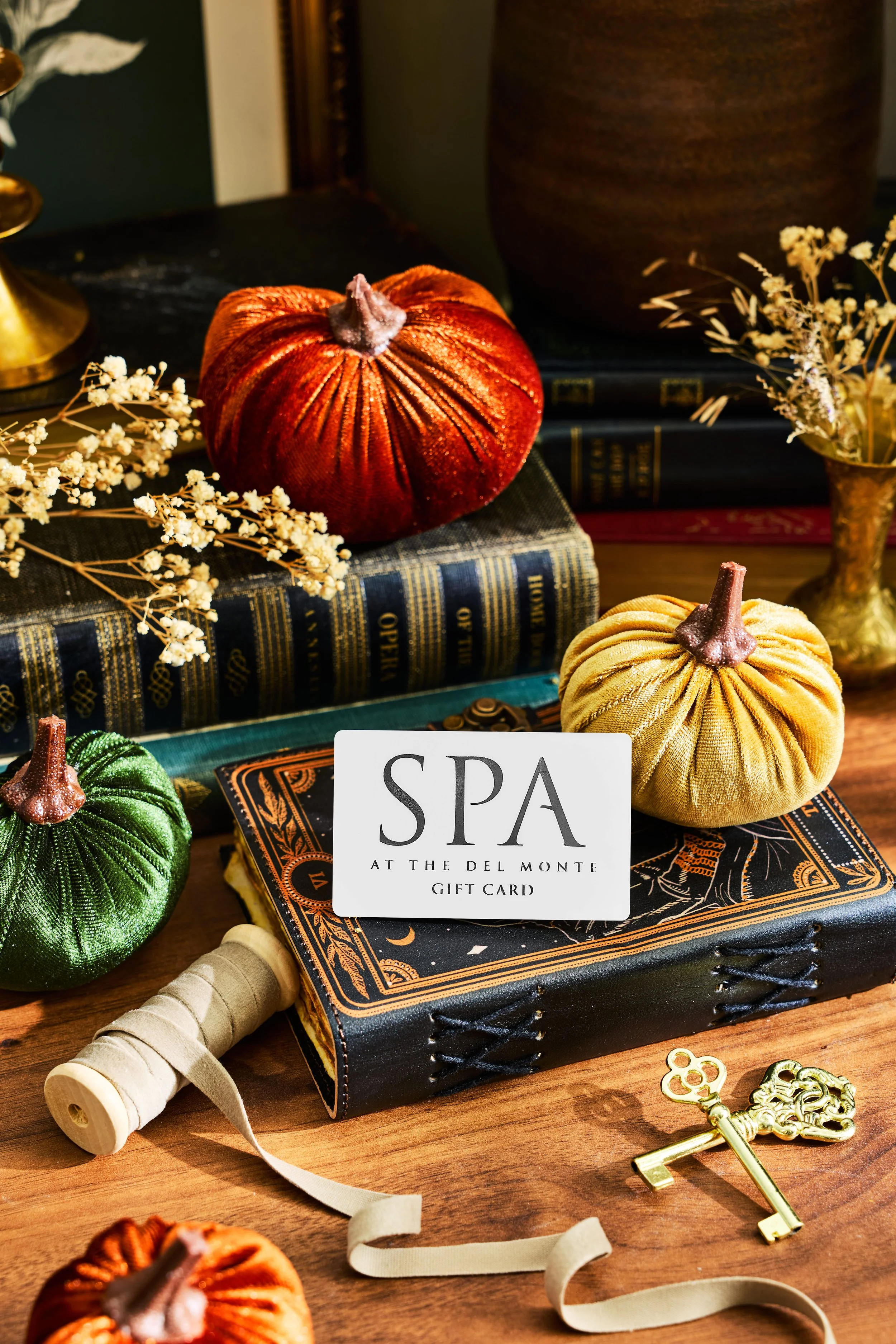 Spa Gift Card laying on top of book next to yellow velvet pumpkins