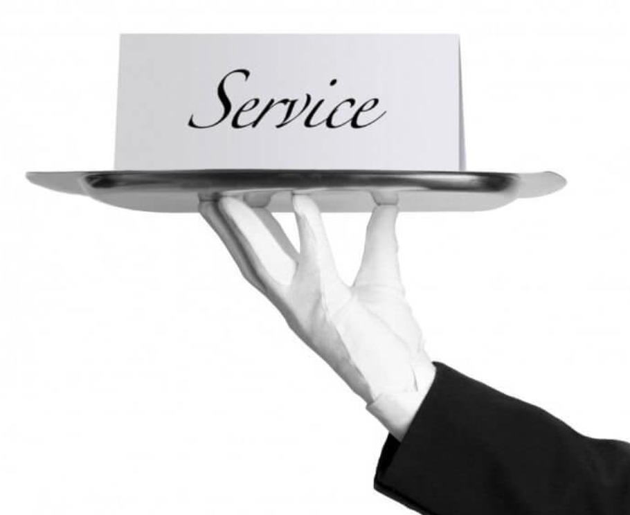A hand in a black suit jacket holding a silver tray with a sign that says 'Service' on it
