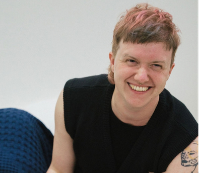 A white smiling person with short blonde hair with pink streaks leaning in