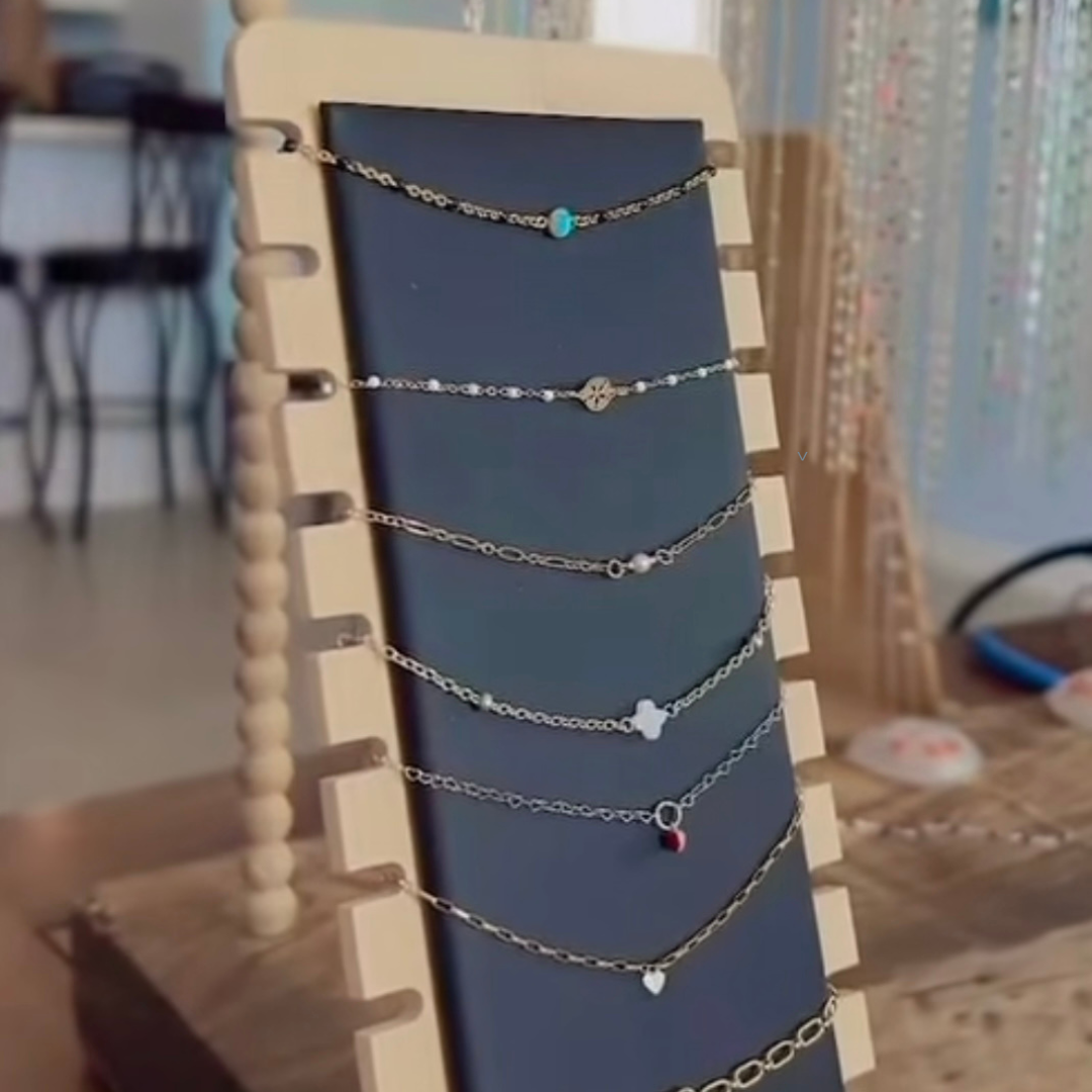 A display stand with multiple silver necklaces featuring various charms and beads, arranged vertically.