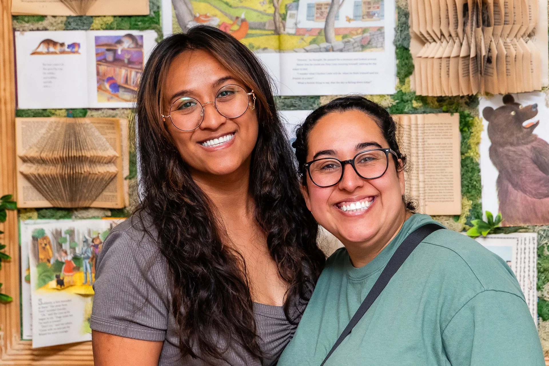 Two smiling women posing in front of a display with books and illustrations about animals.
