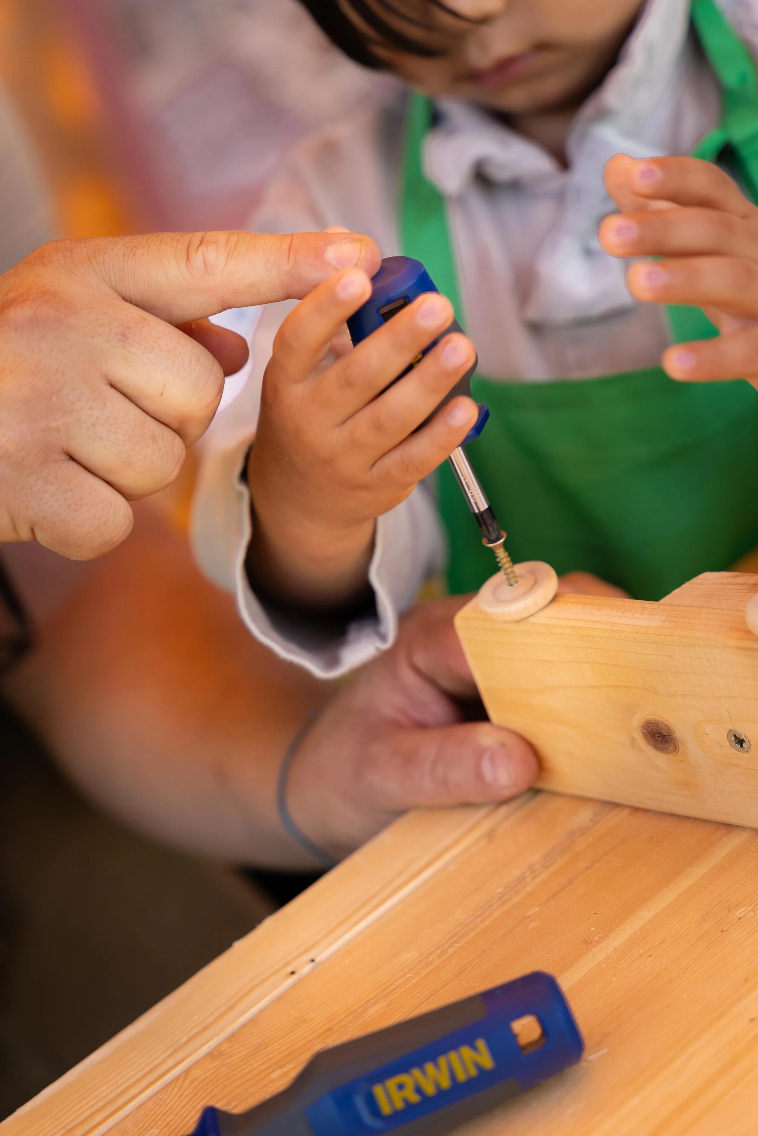 A child and an adult using a screwdriver to insert a screw into a wooden piece.