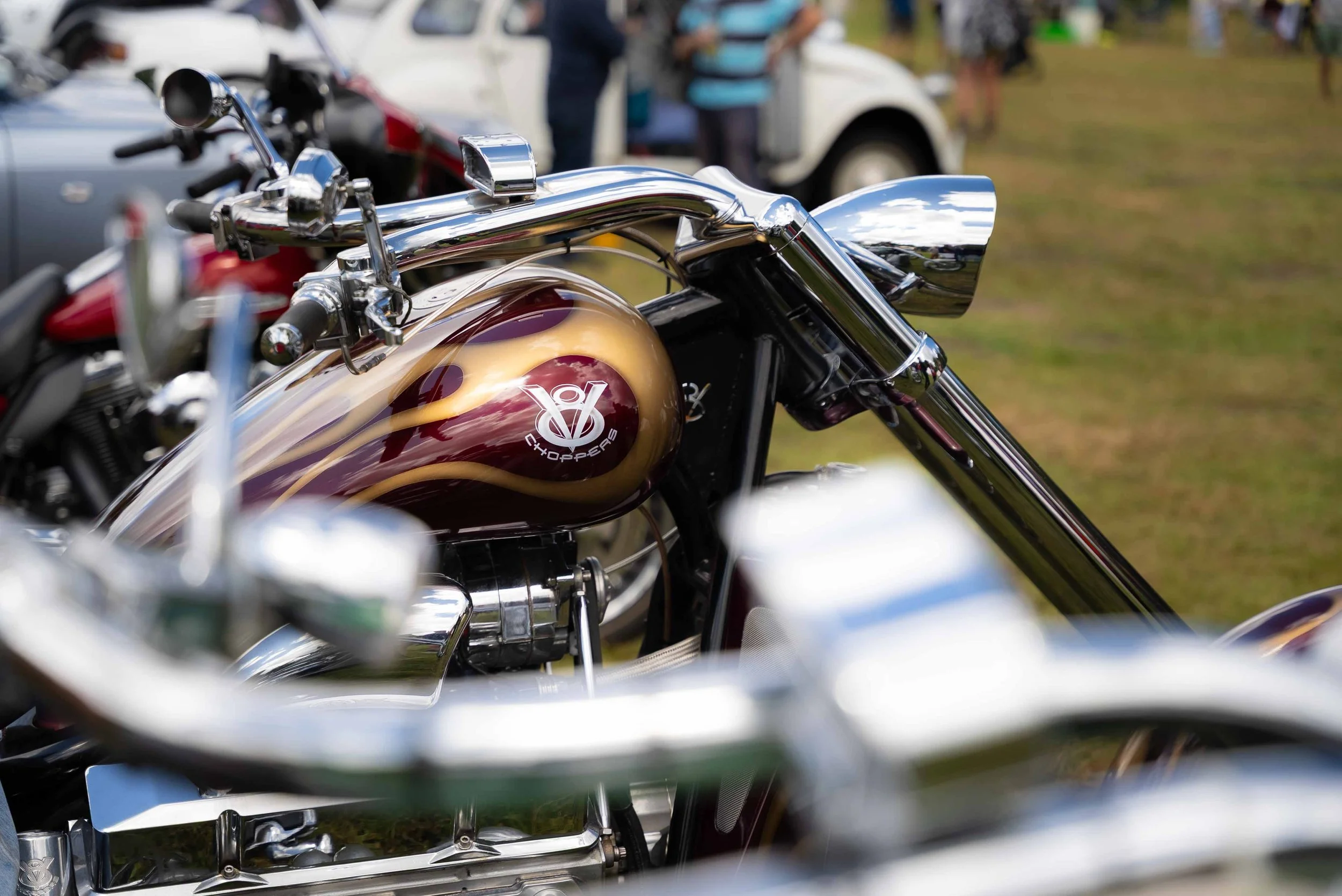 Close-up of a vintage Harley-Davidson motorcycle with metallic paint and chrome details, parked outdoors among other motorcycles and cars.