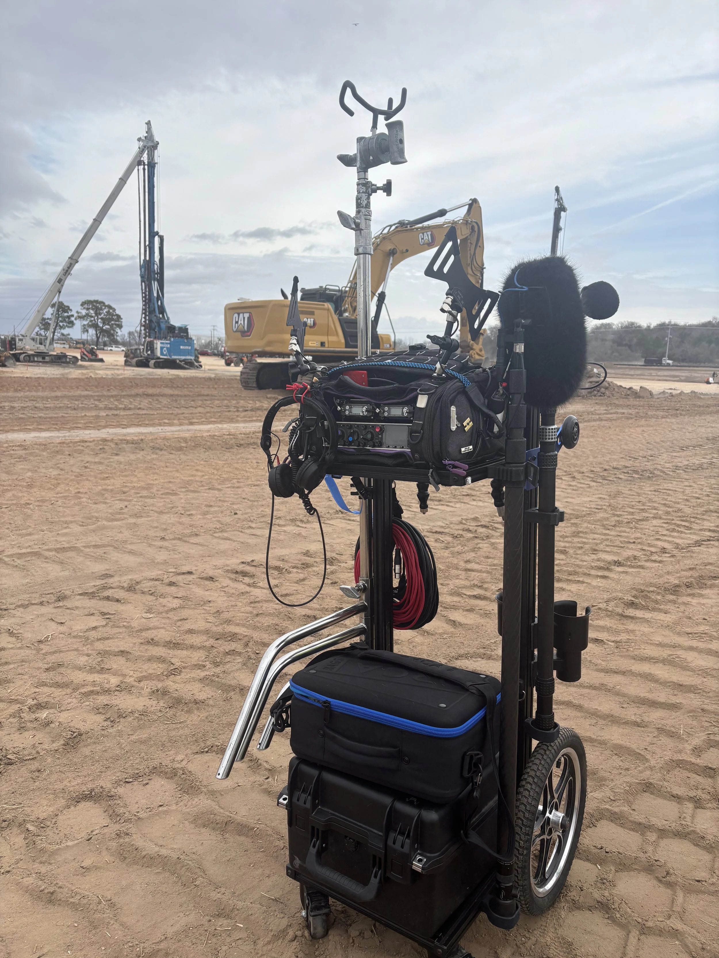 A sound mixer cart with equipment on a construction site with heavy machinery in the background.