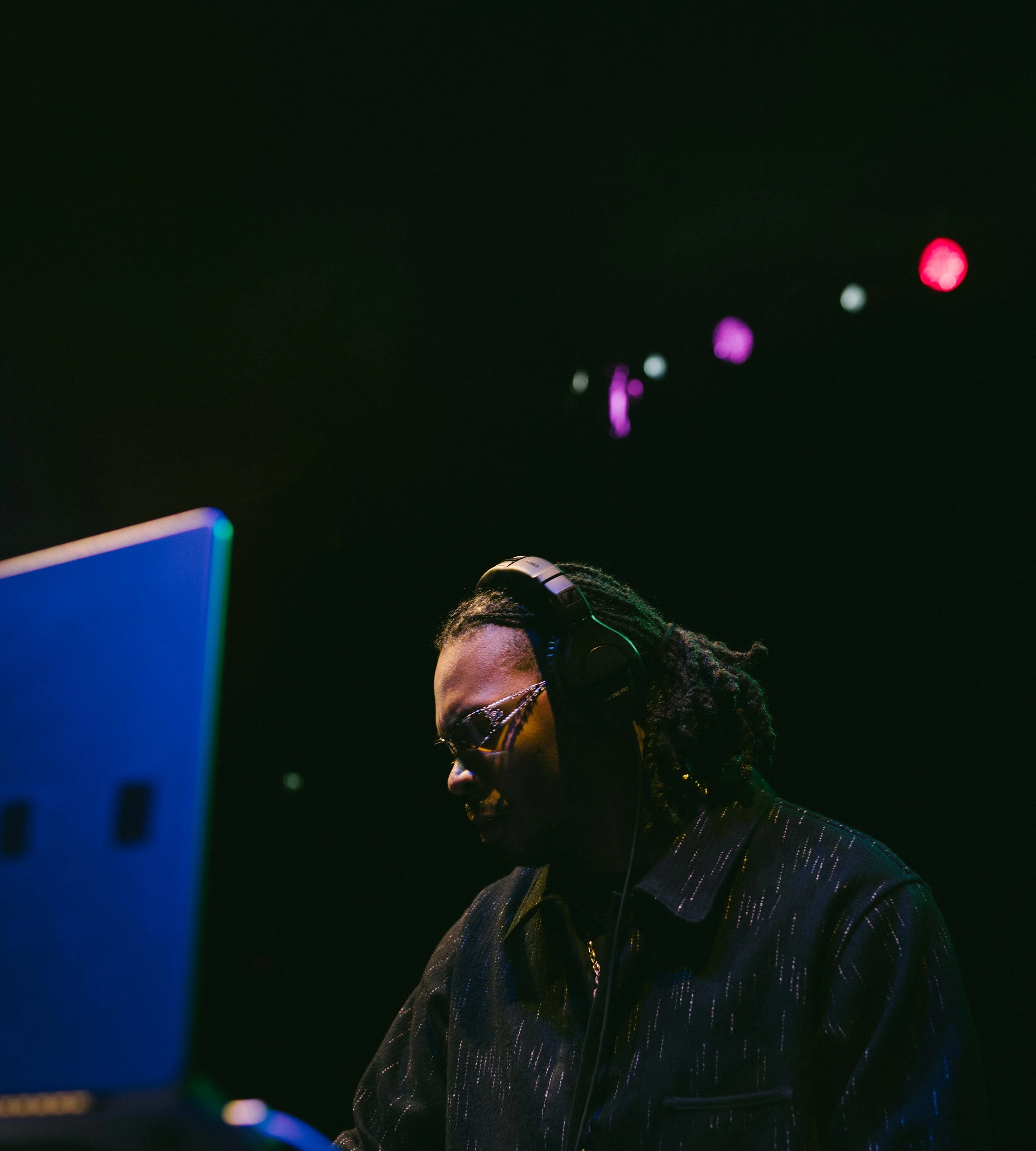 DJ wearing headphones and sunglasses performing at a nightclub with colorful lights in the background.