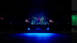 Dark indoor concert venue with stage lights and fog, empty dance floor, and empty seating area.