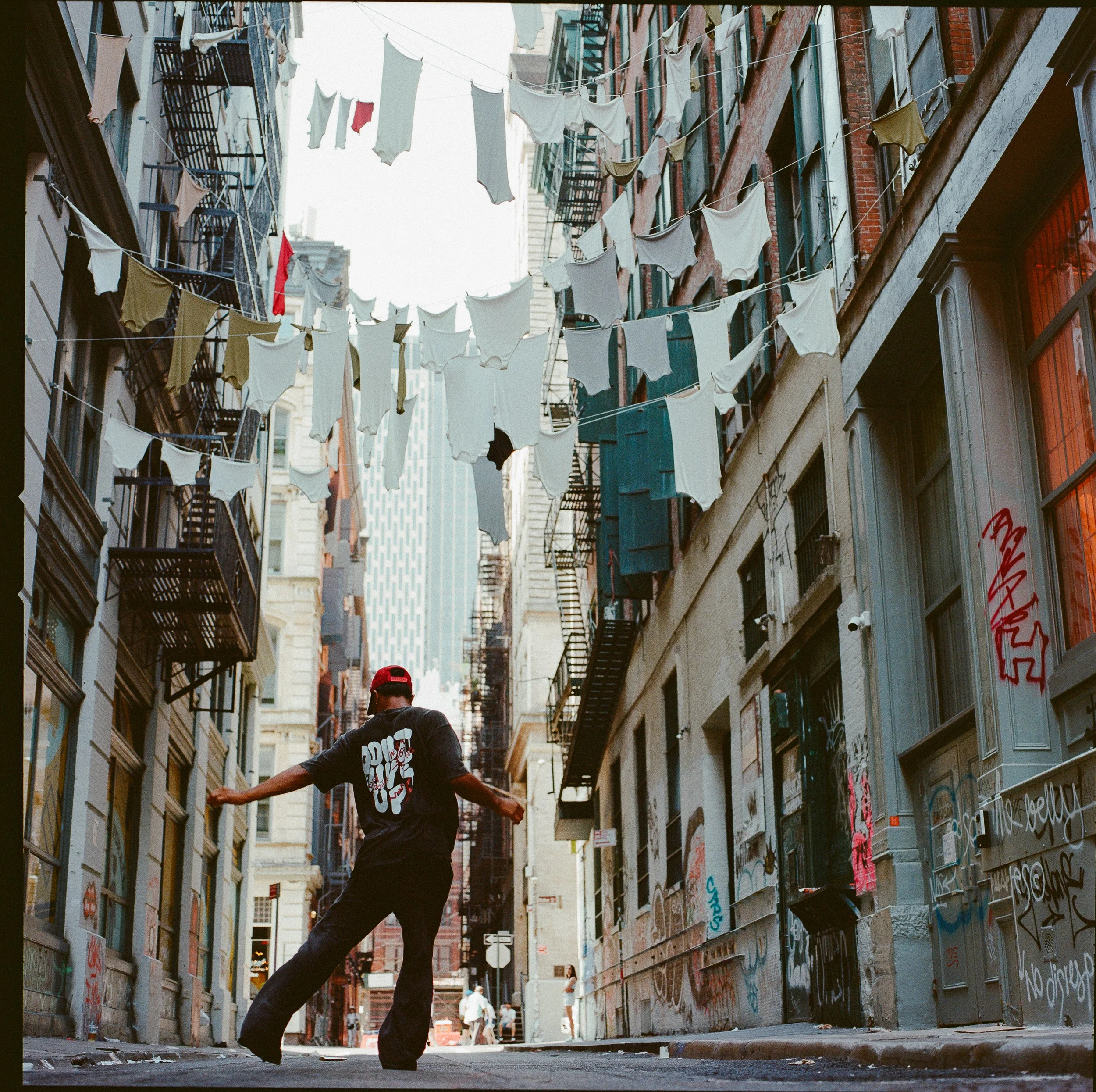 A man dancing in a narrow city alley with laundry hanging between buildings.
