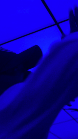 A hand holding a smartphone in a dark room illuminated by blue light.