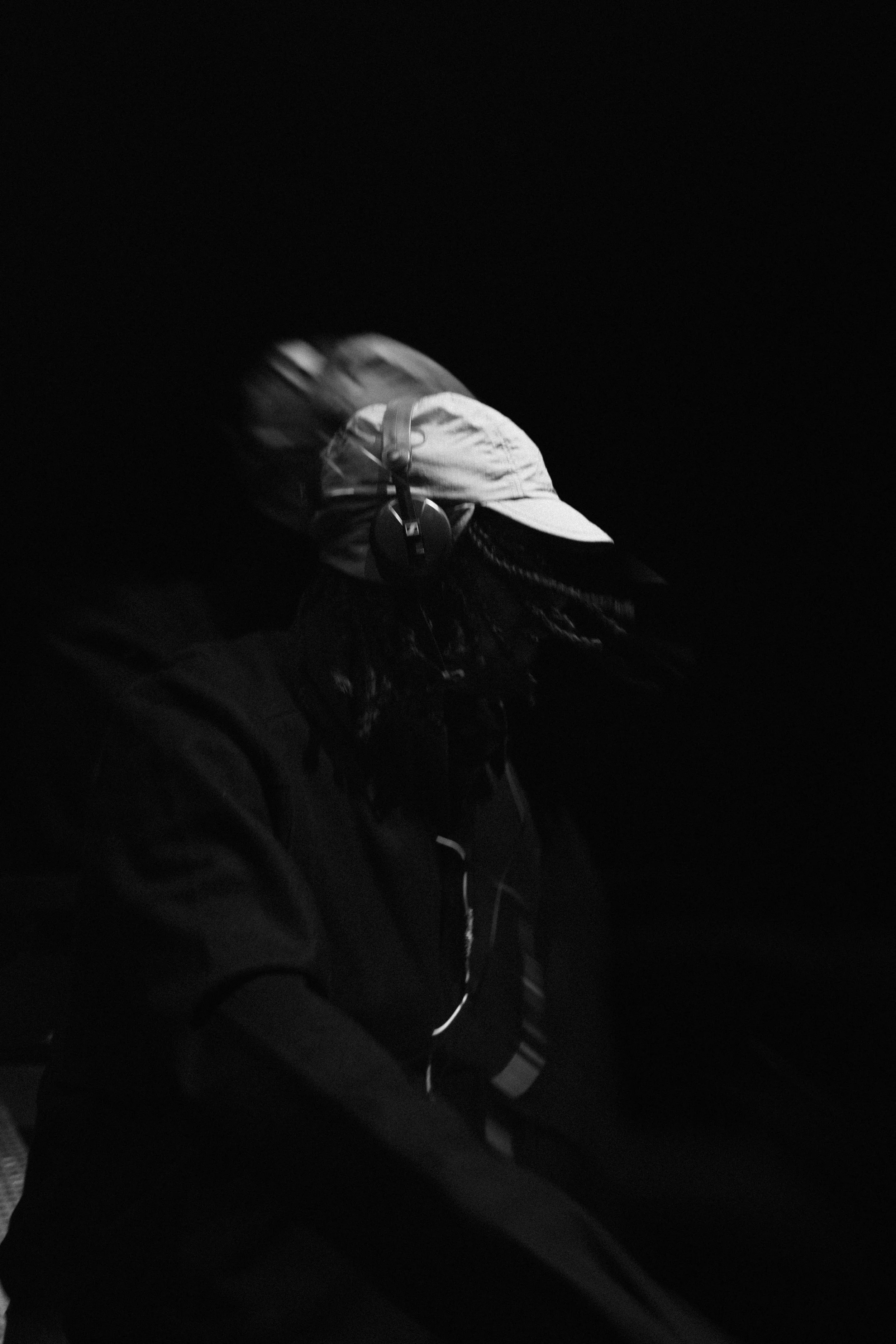 Person wearing a baseball cap, headphones, and dark clothing, captured in a low-light or nighttime setting.