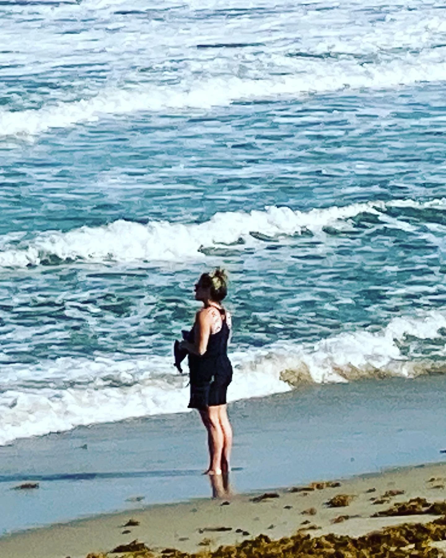 A woman standing on the beach near the ocean shoreline, with waves in the background.