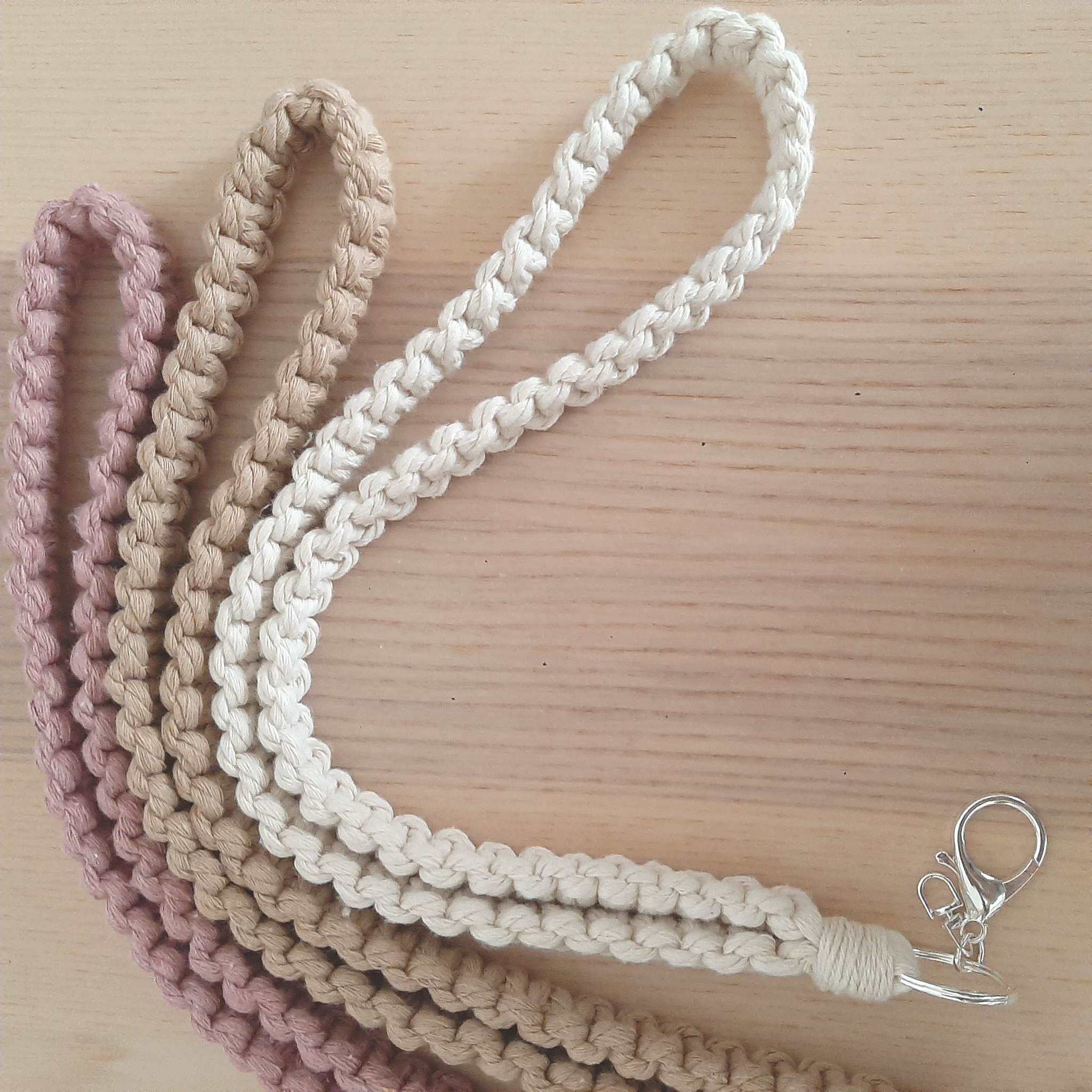 Four braided cotton lanyards in pink, beige, and cream shades on a wooden surface, with a metal clasp on one end.