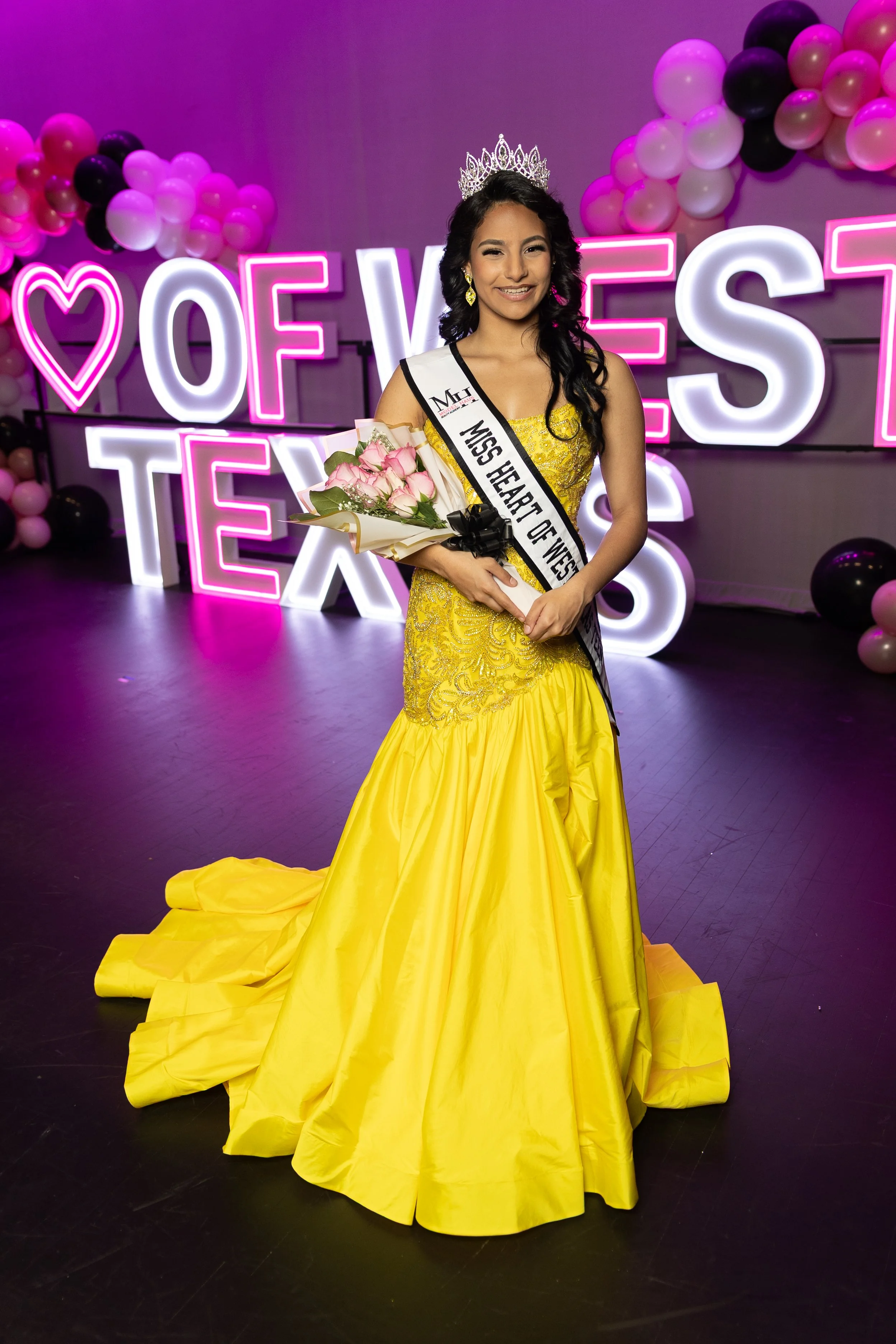 Miss Teen Texas wearing a pink textured dress with a sash and a crown, smiling, against a plain background.