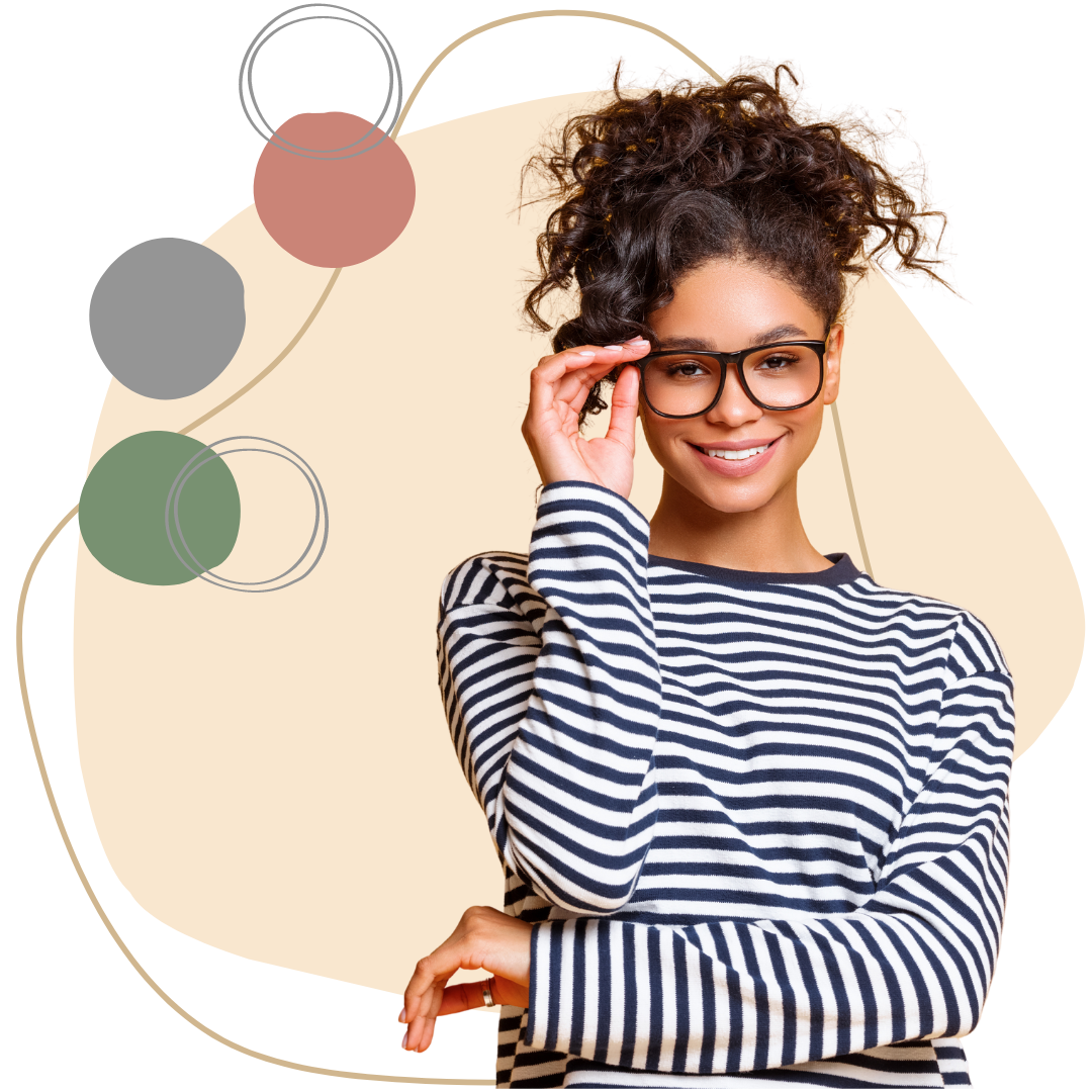 A young woman with curly hair wearing glasses and a striped shirt, smiling and holding her glasses with one hand.