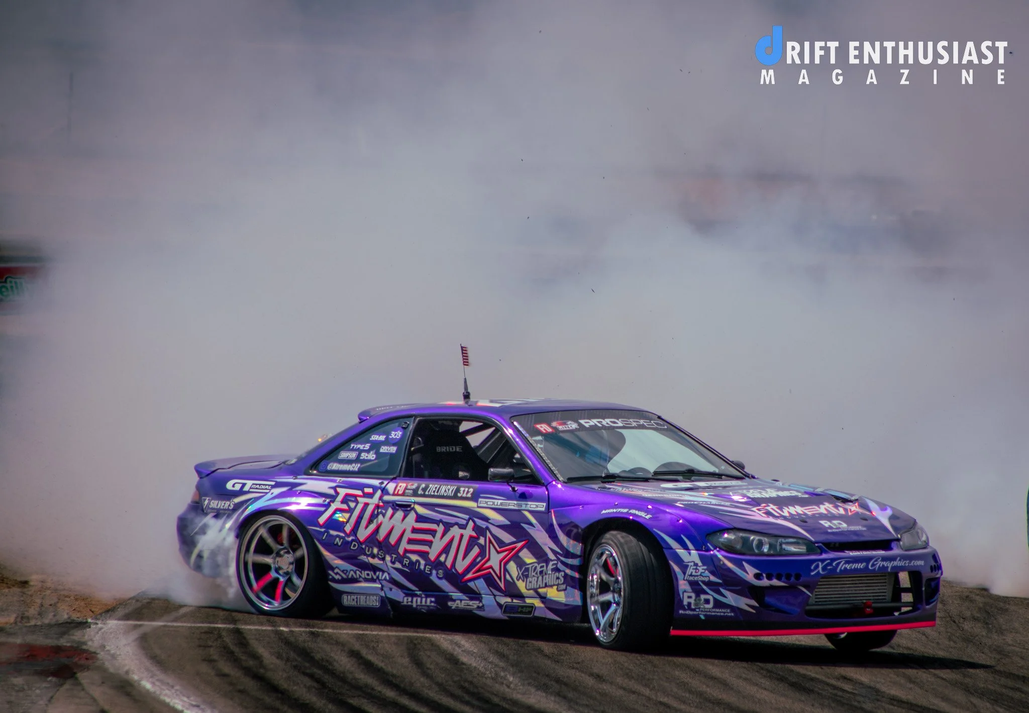 A purple drift car on a racetrack performing a burnout with smoke billowing from the tires, surrounded by track skid marks.