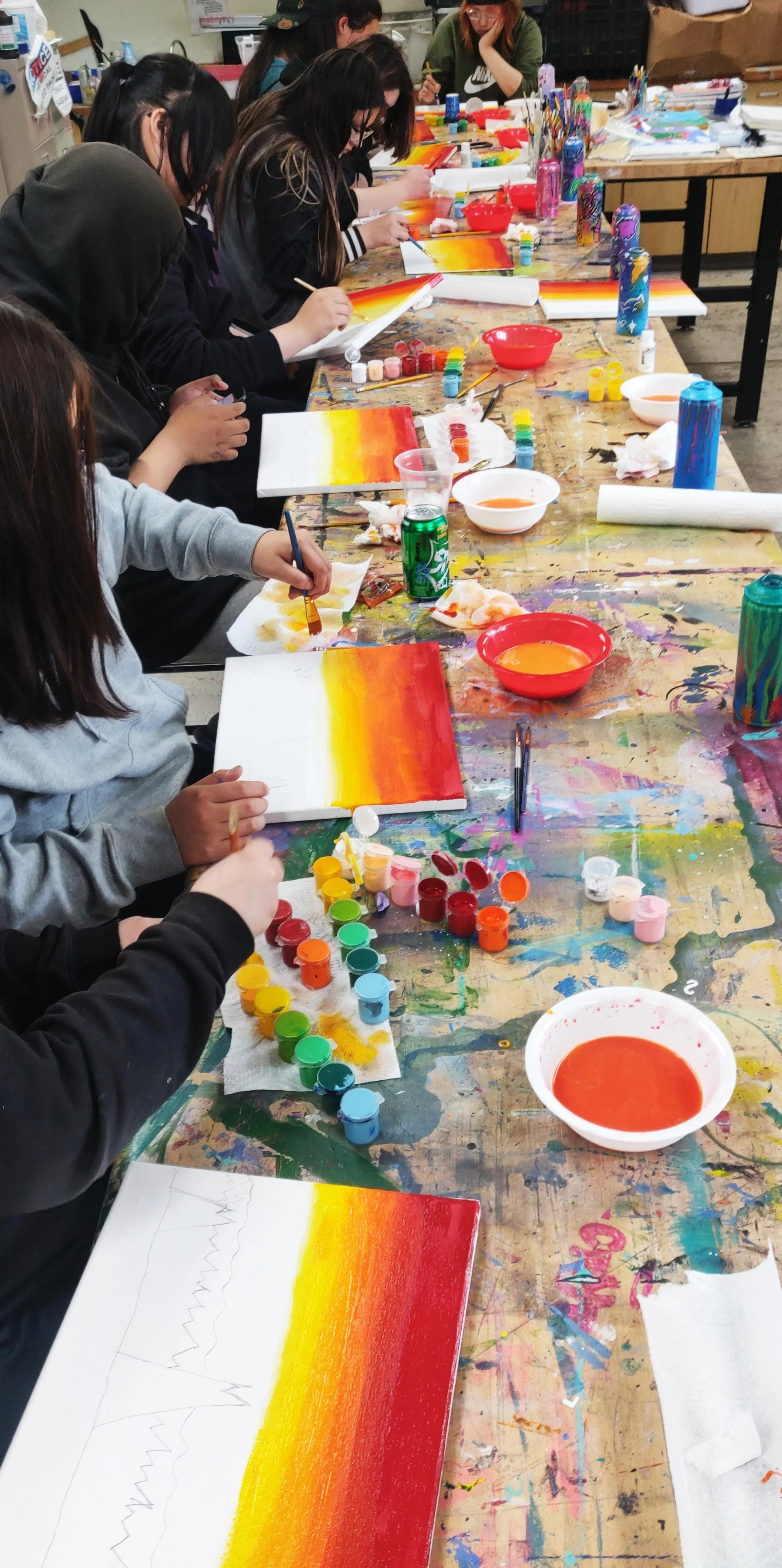 Group painting class with students using vibrant colors on canvases.
