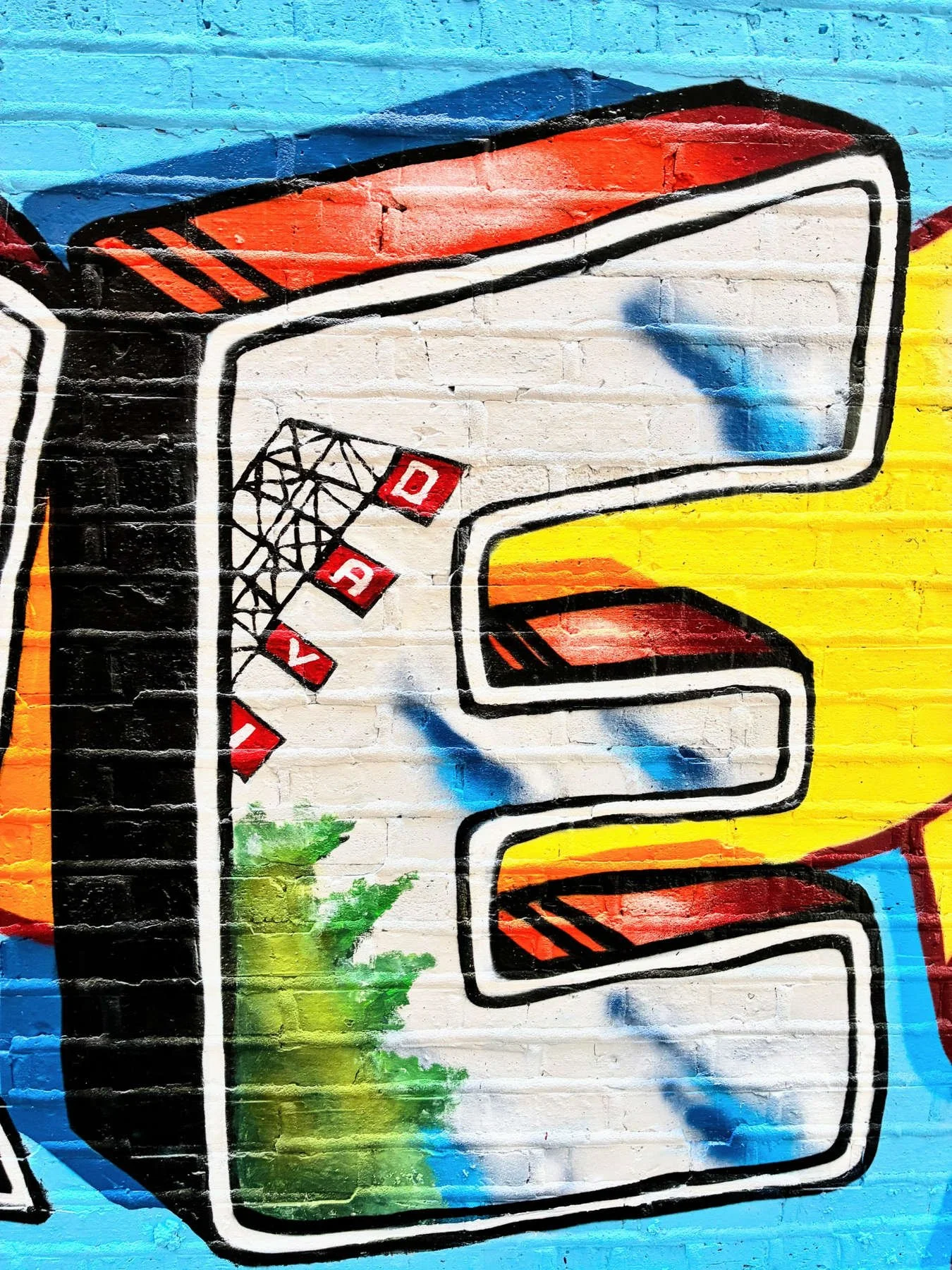 Close-up of the letter E in the Lincoln Square community mural, featuring the Chicago elevated train tracks and colorful graffiti-style lettering on a blue brick wall.