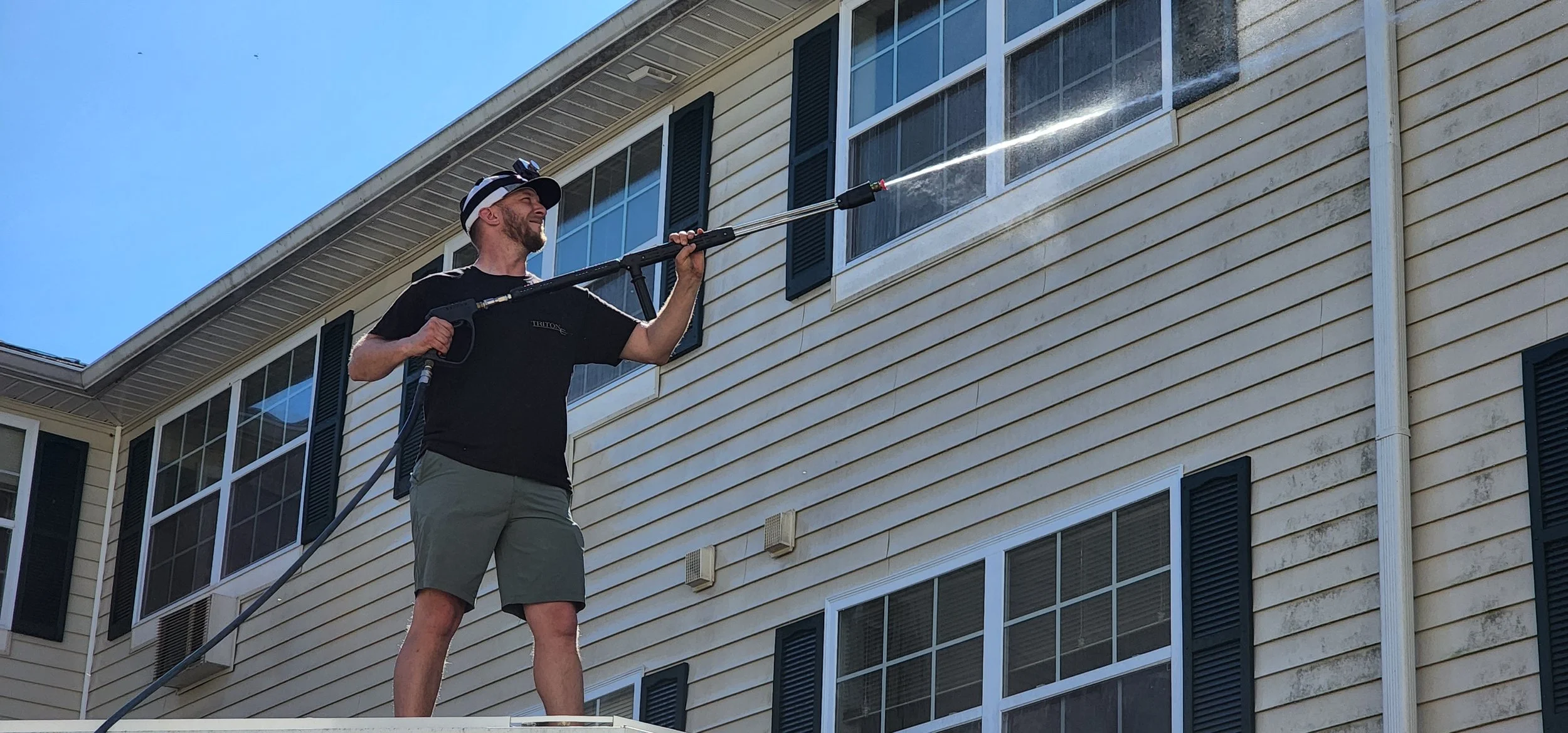 Triton Cleaning Services employee soft washing siding.