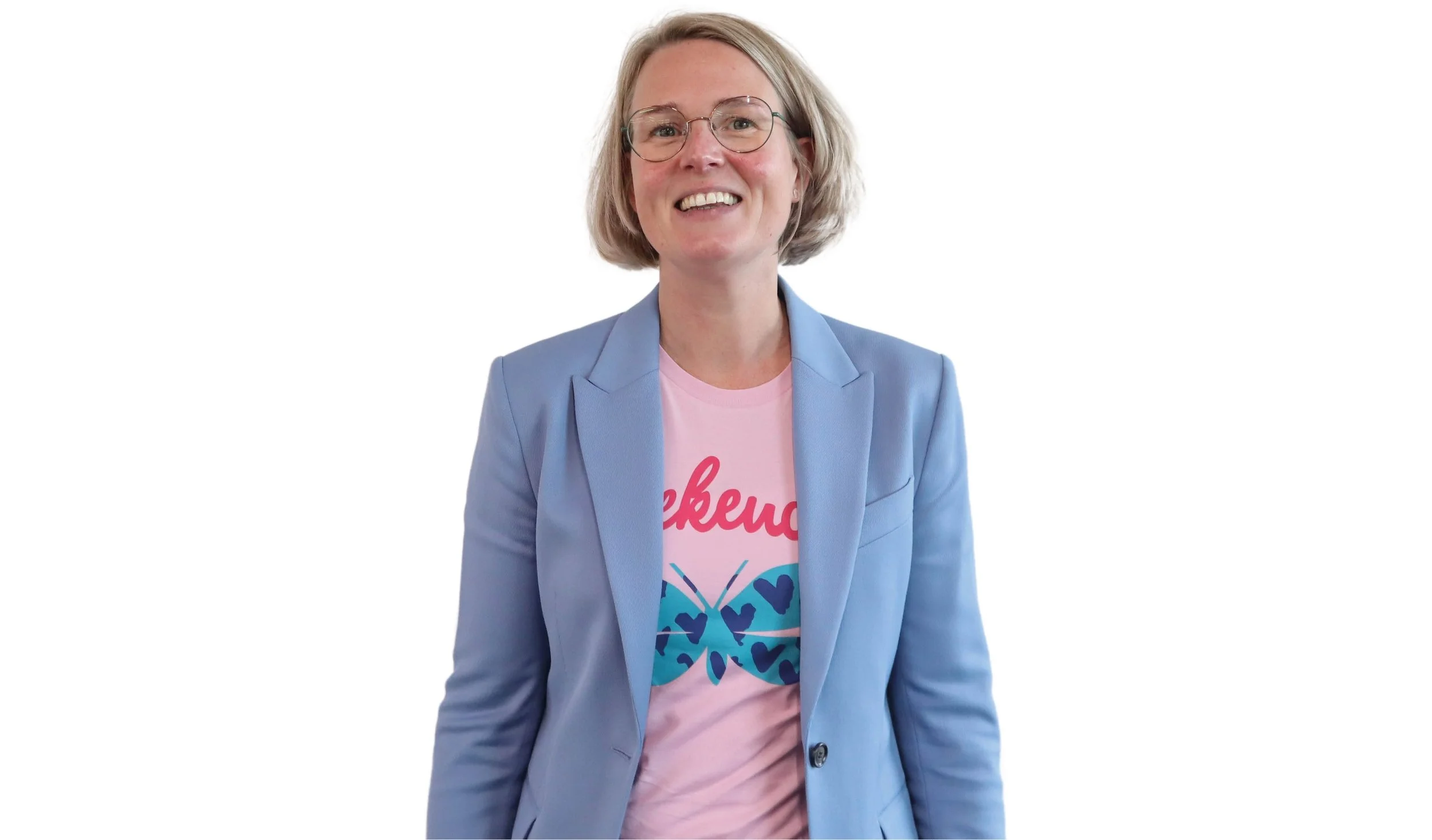 A middle-aged woman with short blond hair, glasses, wearing a light blue blazer over a pink graphic T-shirt with a butterfly and the word 'awake' playful font, smiling against a white background.