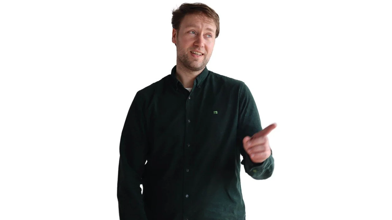 A man in a black shirt is pointing and making a face suggesting he is explaining or emphasizing something.