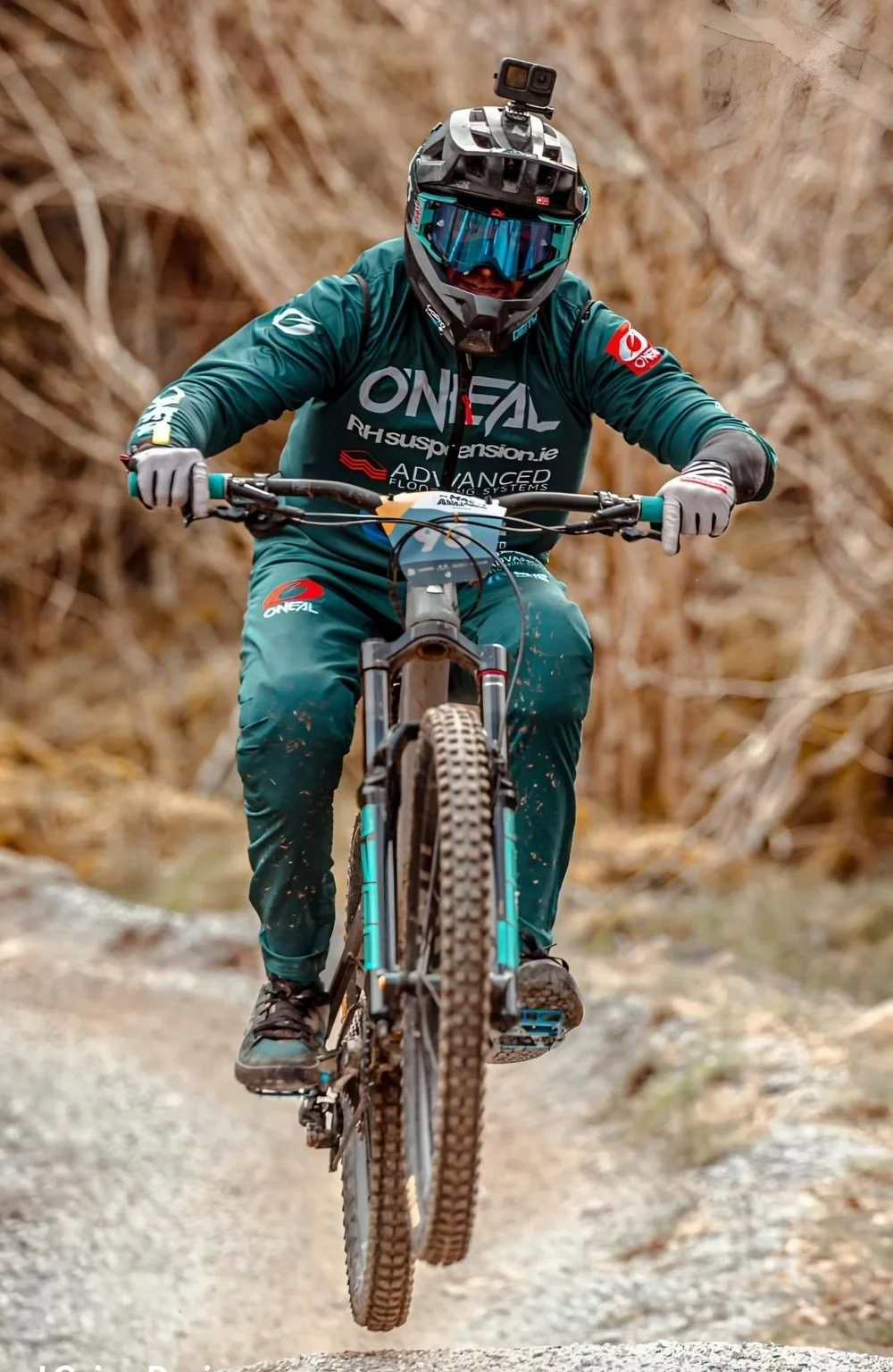 Mountain biker wearing a helmet and goggles riding on a dirt trail with a blurred natural background.