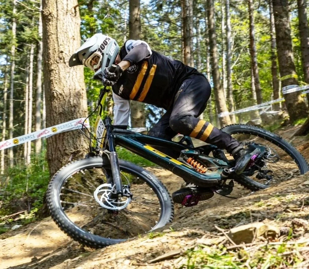 Mountain biker wearing a helmet and black protective gear navigating a dirt trail through a forest.