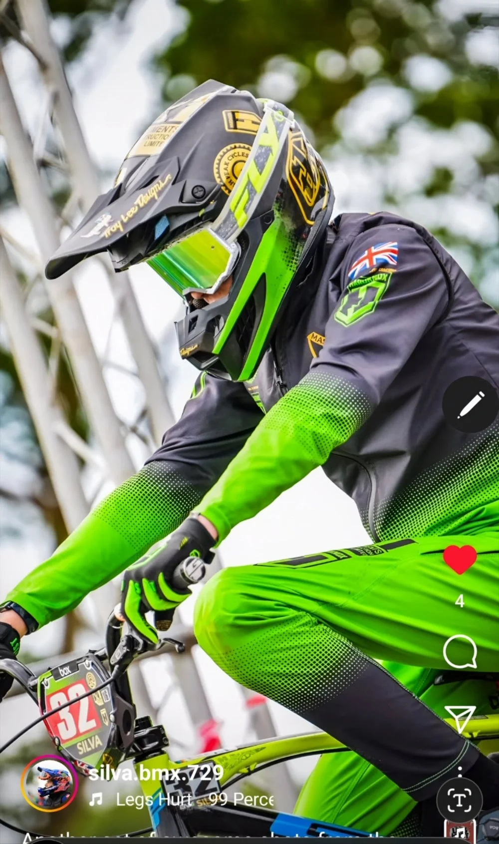 Close-up of a BMX cyclist in green and black gear with a helmet and reflective goggles, riding a yellow bike marked with the number 32.