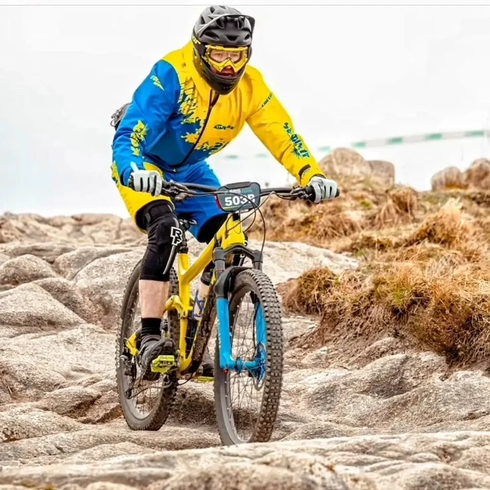 Mountain biker wearing a yellow and blue outfit with a helmet and goggles rides over rocky terrain on a yellow and black bike.