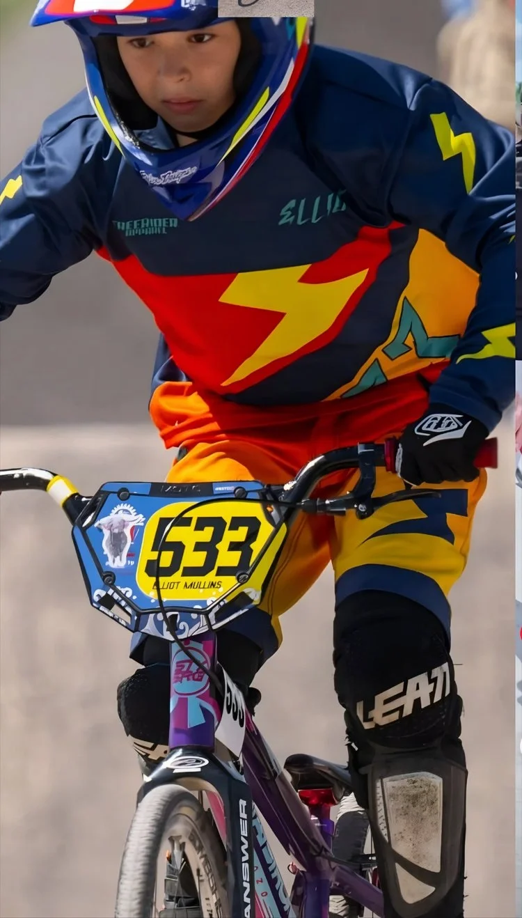 A young person riding a purple mountain bike with a yellow number plate 5333, wearing bright orange pants, a dark blue and red bmx jersey, a blue helmet, and black gloves.