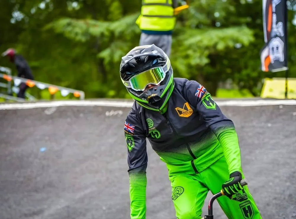 BMX rider wearing black and green gear, helmet, and goggles on a BMX Track