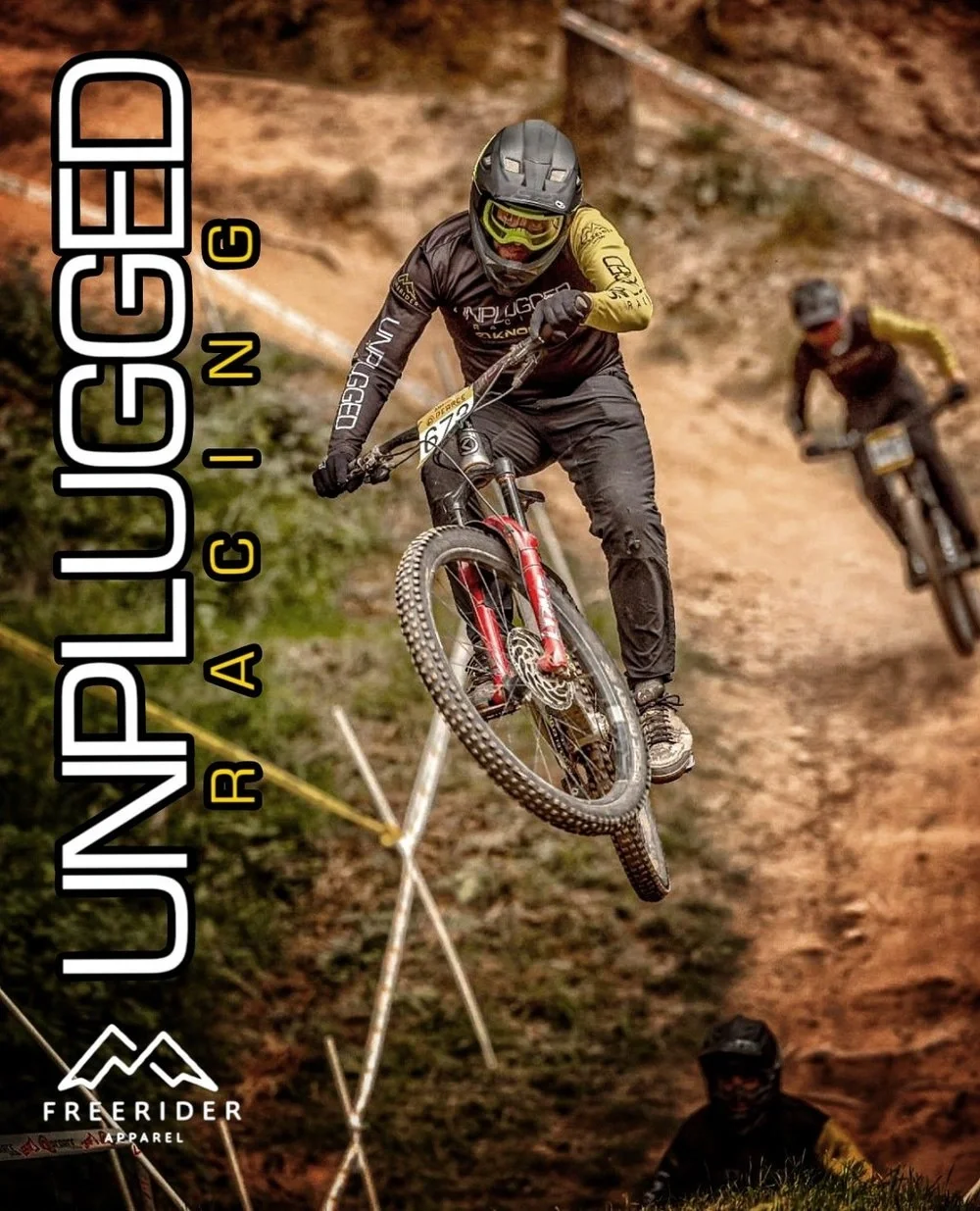 A mountain biker in mid-air executing a jump on a dirt trail, with two other bikers in the background on a rugged outdoor trail.