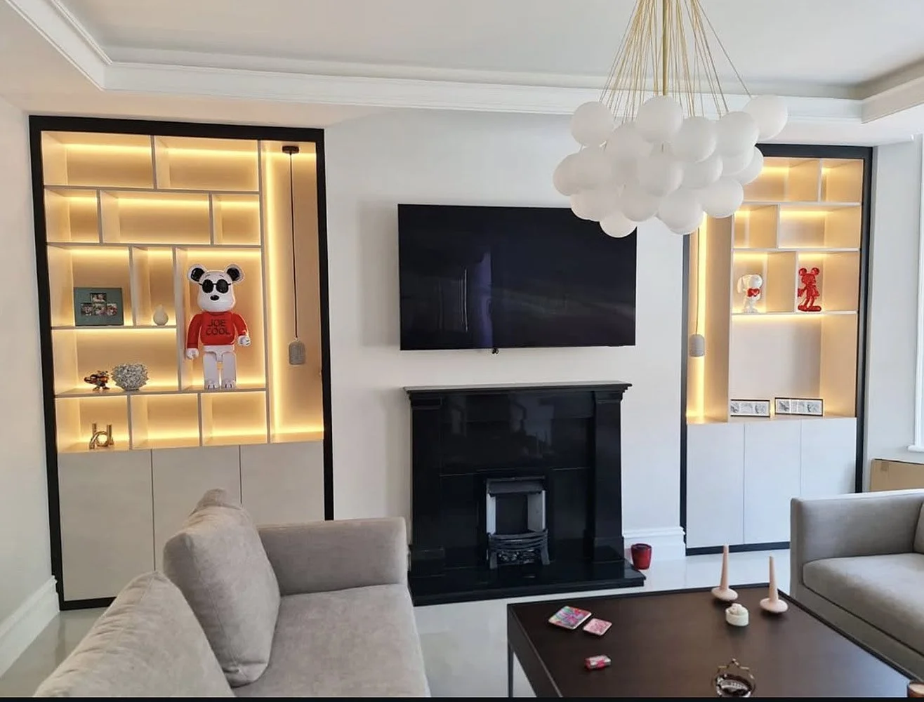 A made-to-measure living room storage solution combining illuminated display shelving, concealed cupboards and modern fitted furniture.