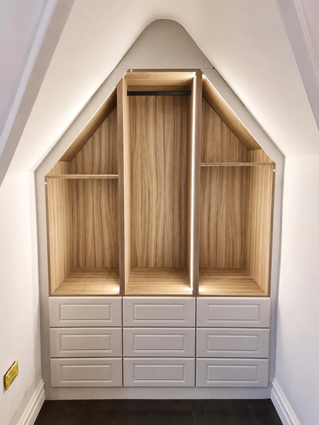 A bespoke angled alcove wardrobe featuring warm oak interiors, integrated LED lighting and tailored storage designed to maximise an awkward space.